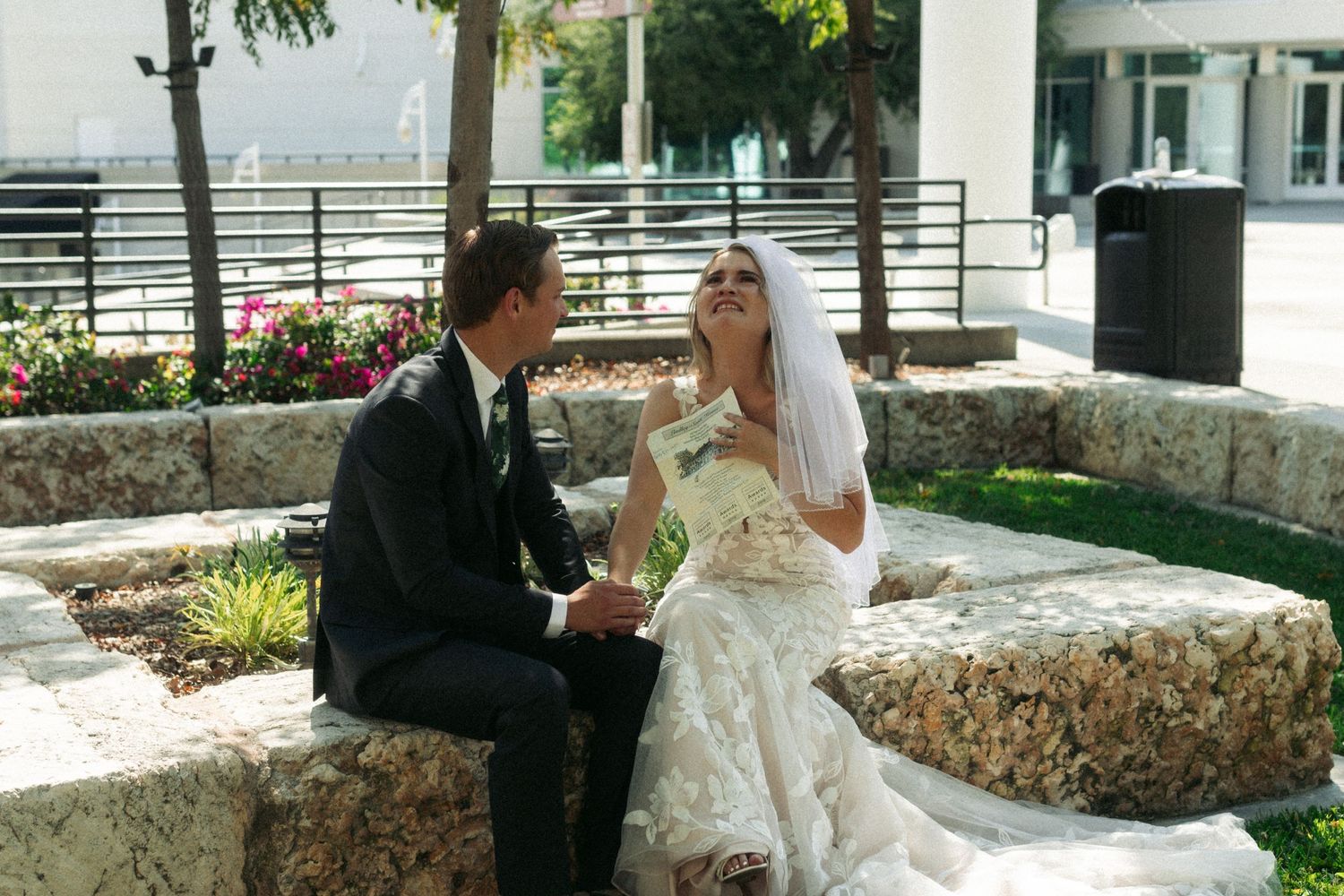 An emotional bride and groom sitting on a stone wall together on a sunny day reading each other vows. Documentary/ photojournalist photos