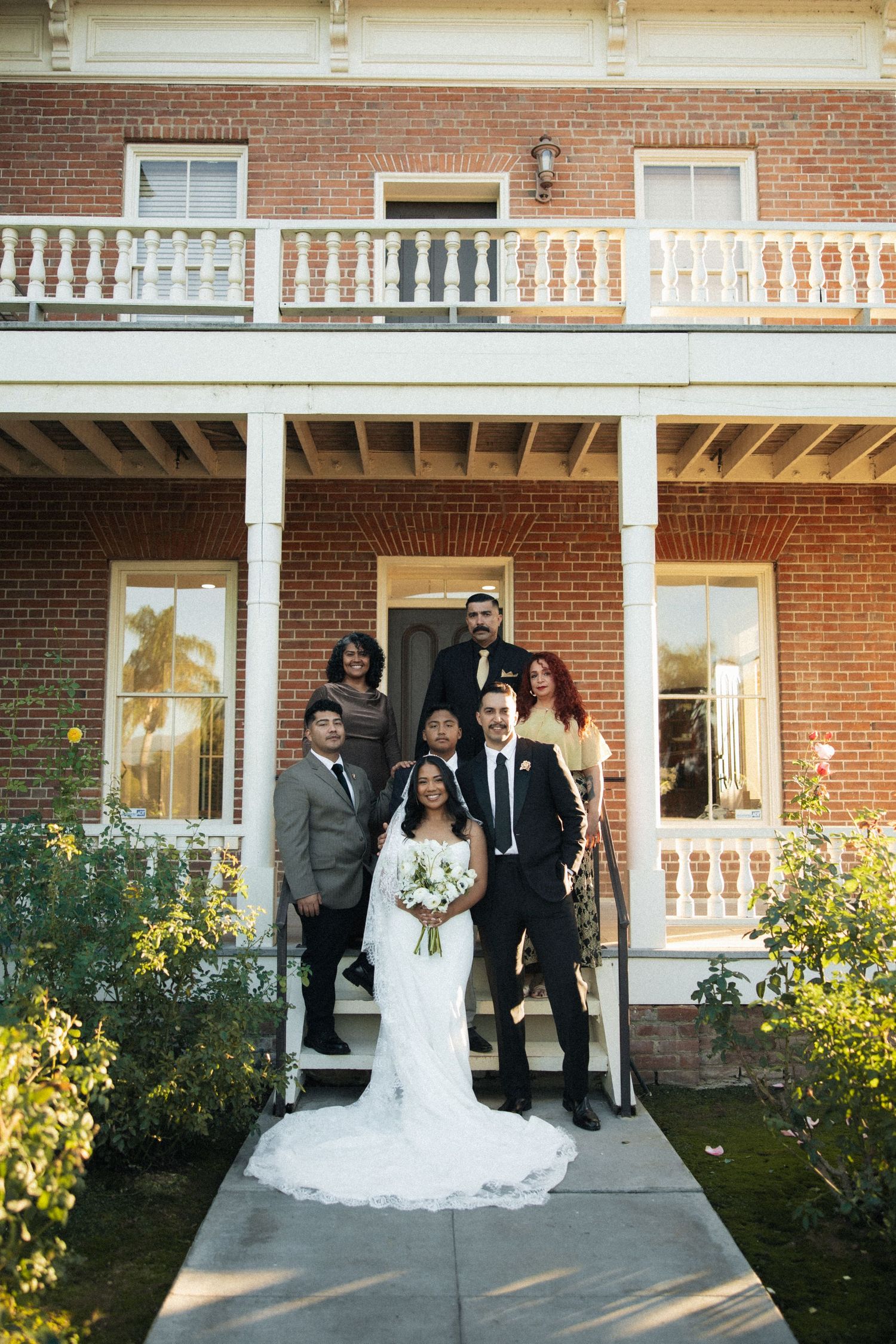 Wedding party poses in front of a classic red brick mansion with white columns and balustrade.