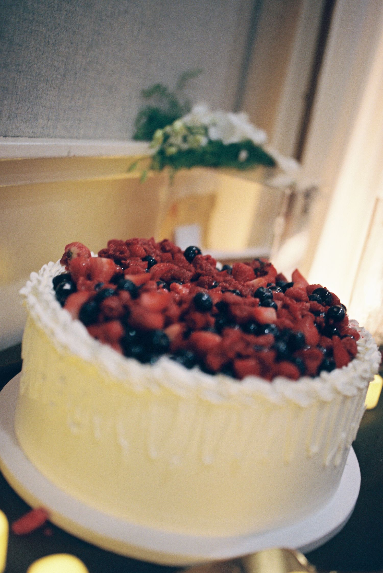 A white cheesecake topped with fresh strawberries and blueberries is shown from multiple angles.