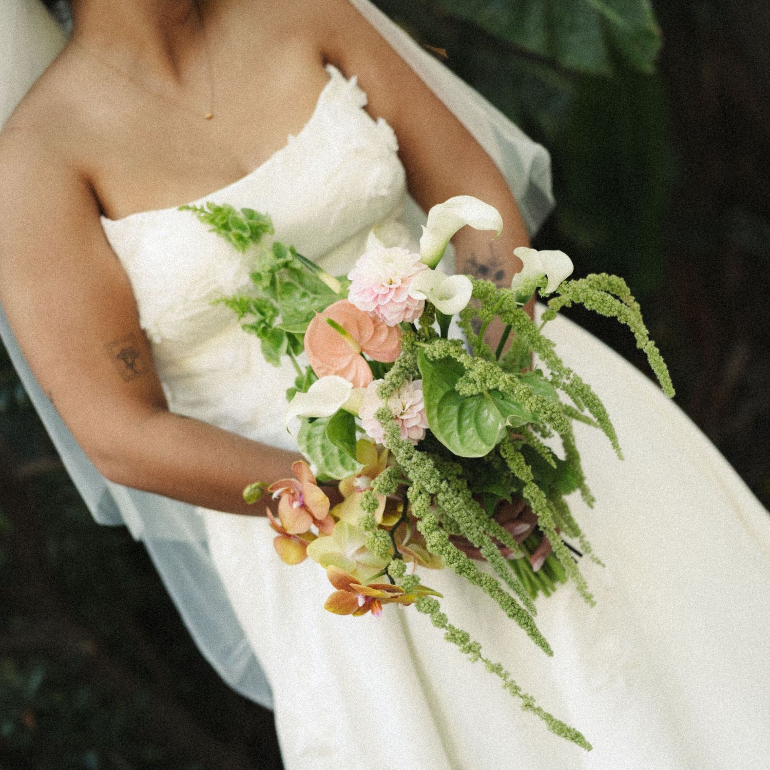 Bride in strapless white gown holding lush cascading bouquet with ferns, pink blooms, and greenery.