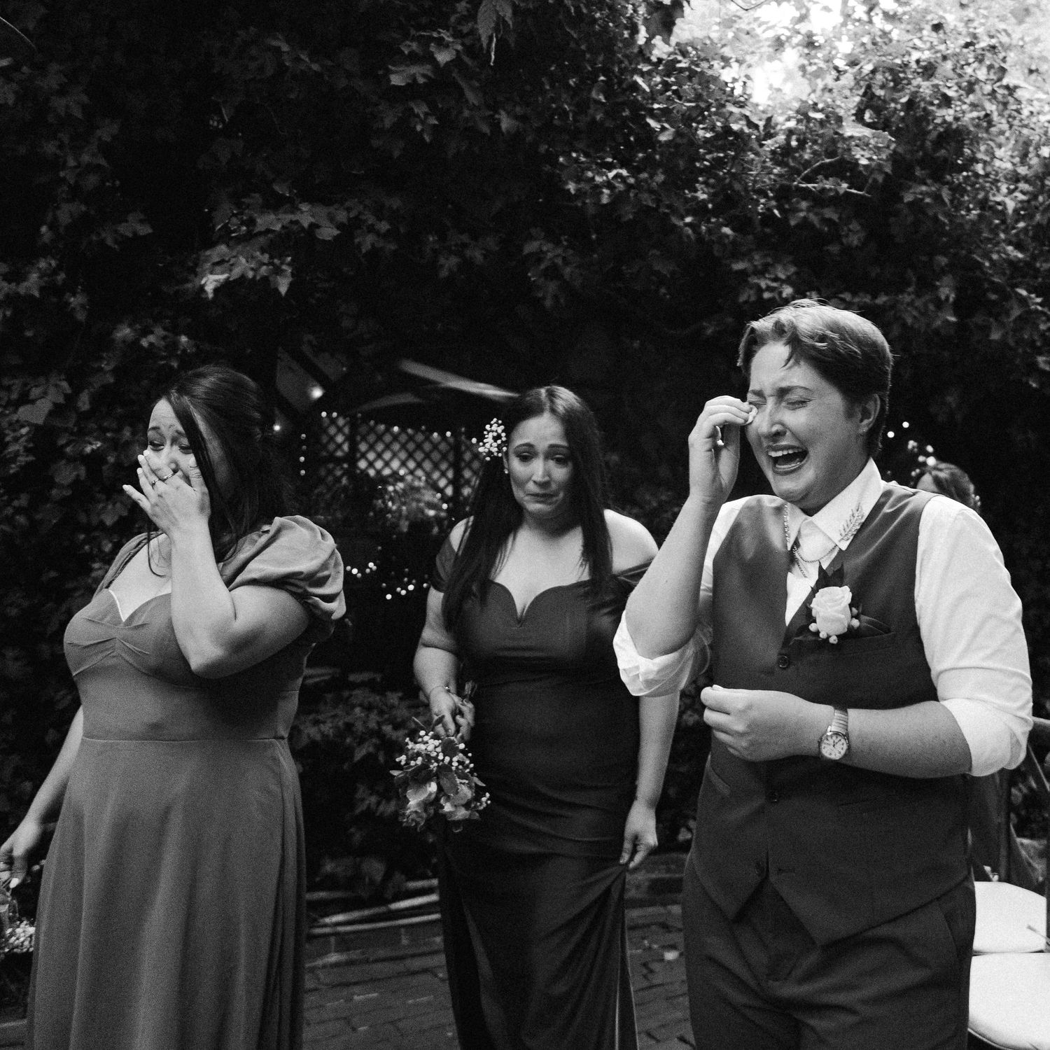 Wedding party members laugh while covering their ears during outdoor celebration in black and white photography.