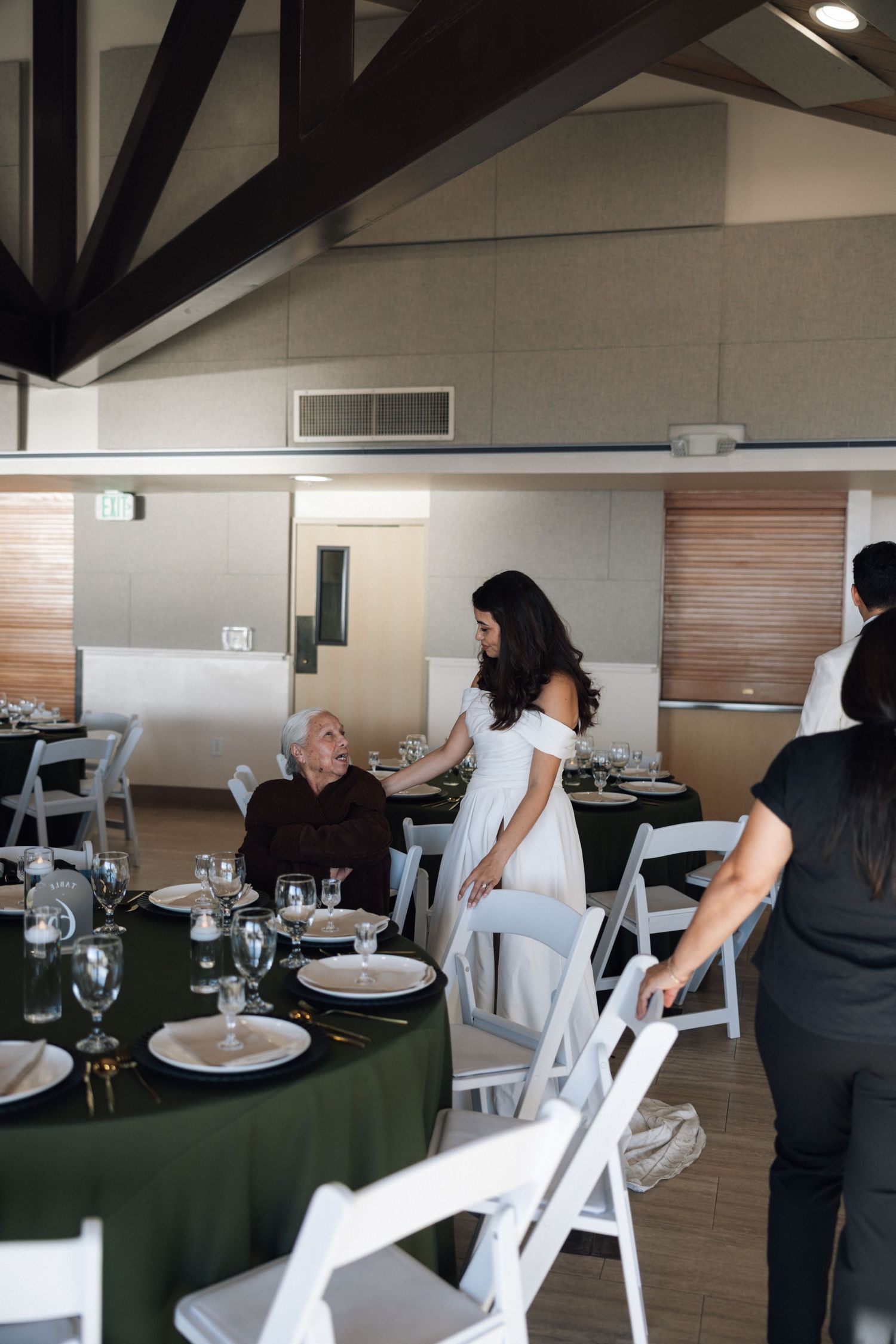 Banquet hall setup with white folding chairs and round tables covered in dark green tablecloths.