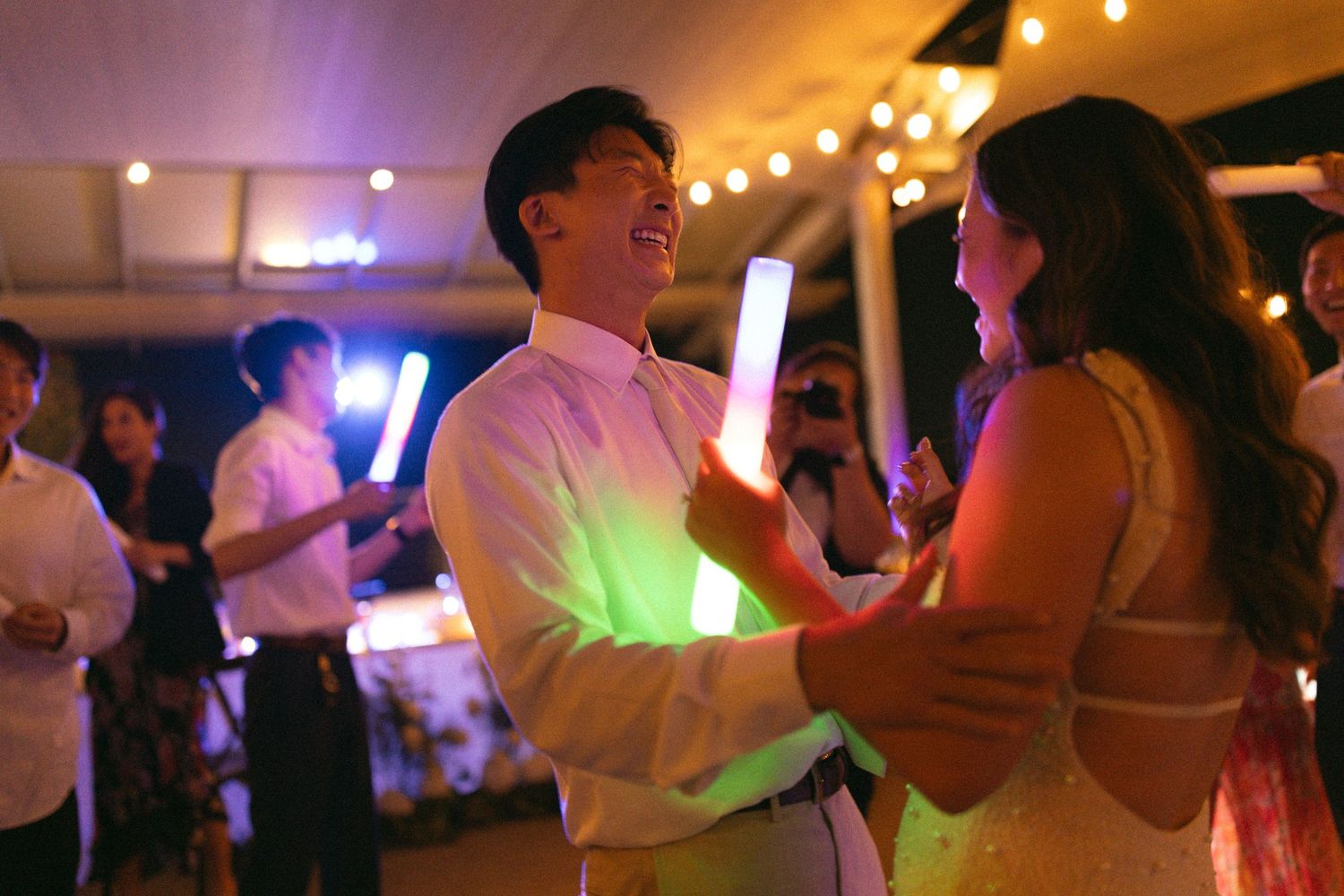 A couple dances at a party under warm string lights  creating a festive atmosphere. Documentary/ photojournalist photography