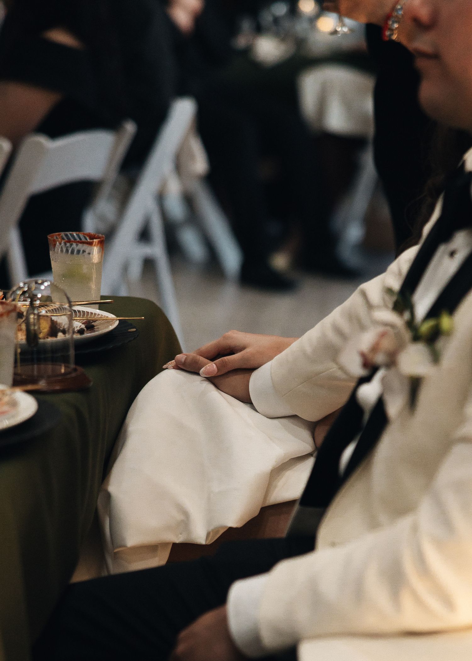 Guests in formal attire seated at a dimly lit event take notes with pens during a presentation or meeting.