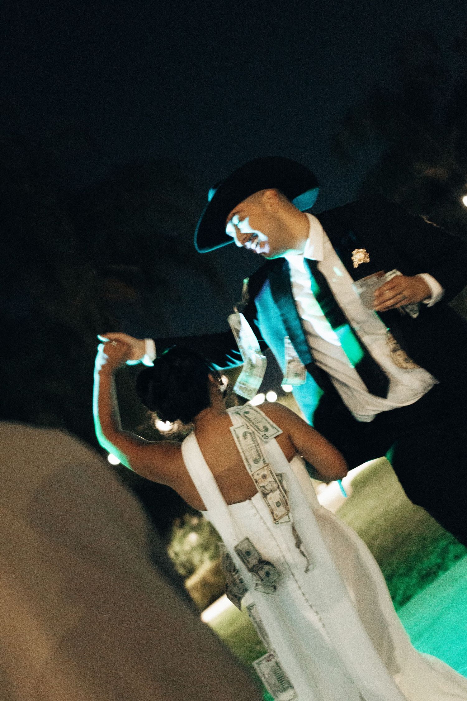 A couple dances together at a nighttime event with turquoise lighting illuminating their formal attire.
