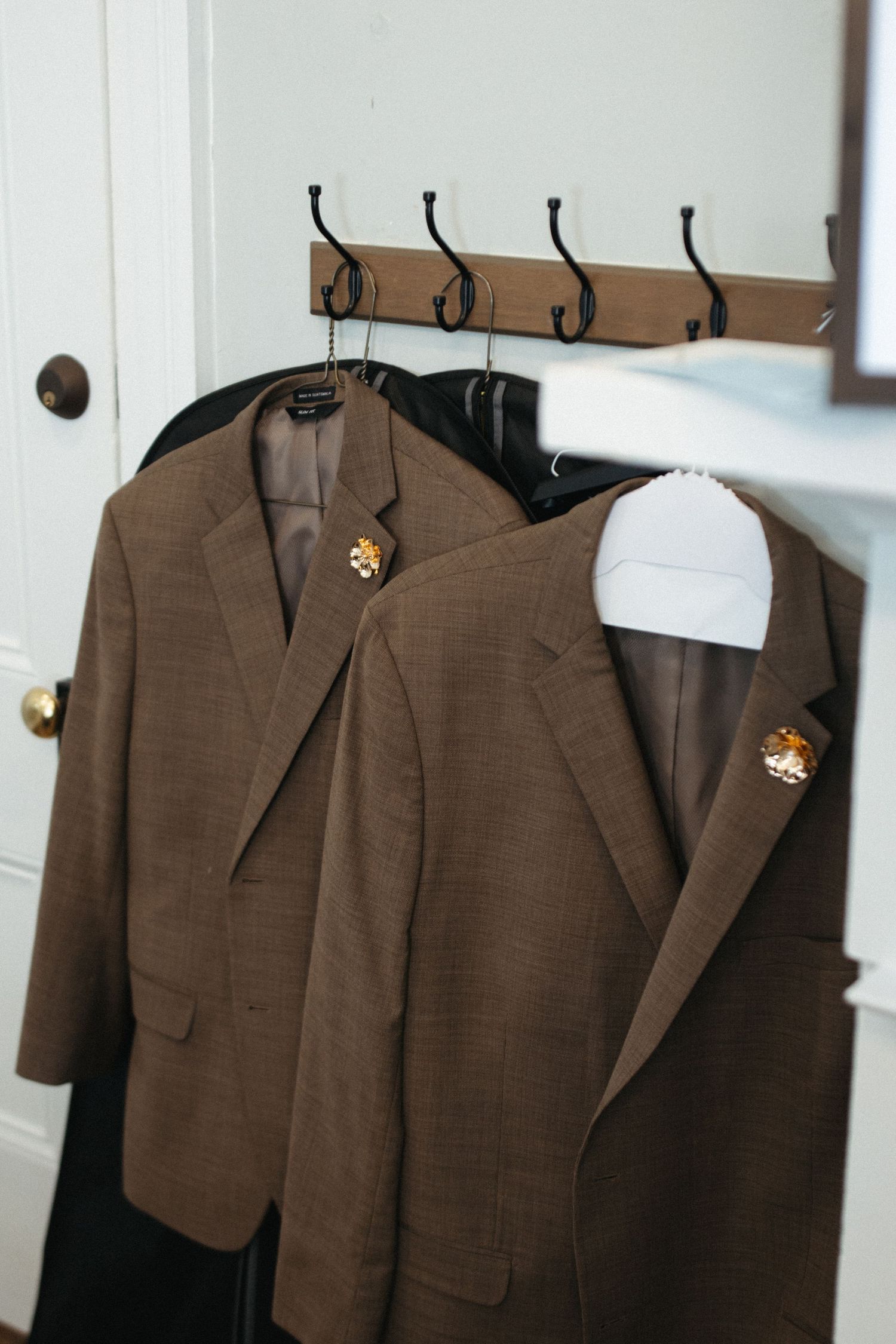 Brown suit jackets hanging on hooks against a white wall display classic menswear organization.