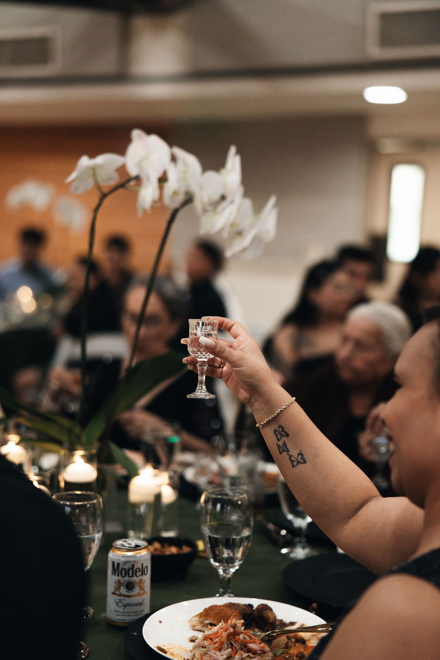 People enjoying drinks and food at an elegant dinner party with white orchids and ambient lighting.