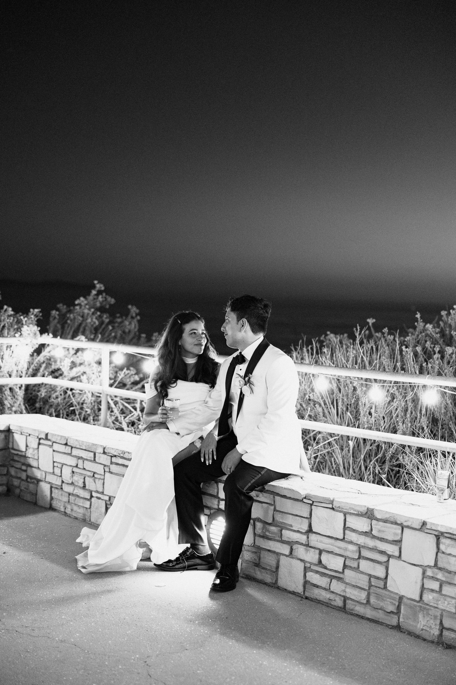 A romantic black and white wedding photo sequence showing a couple dancing along a stone wall at sunset.