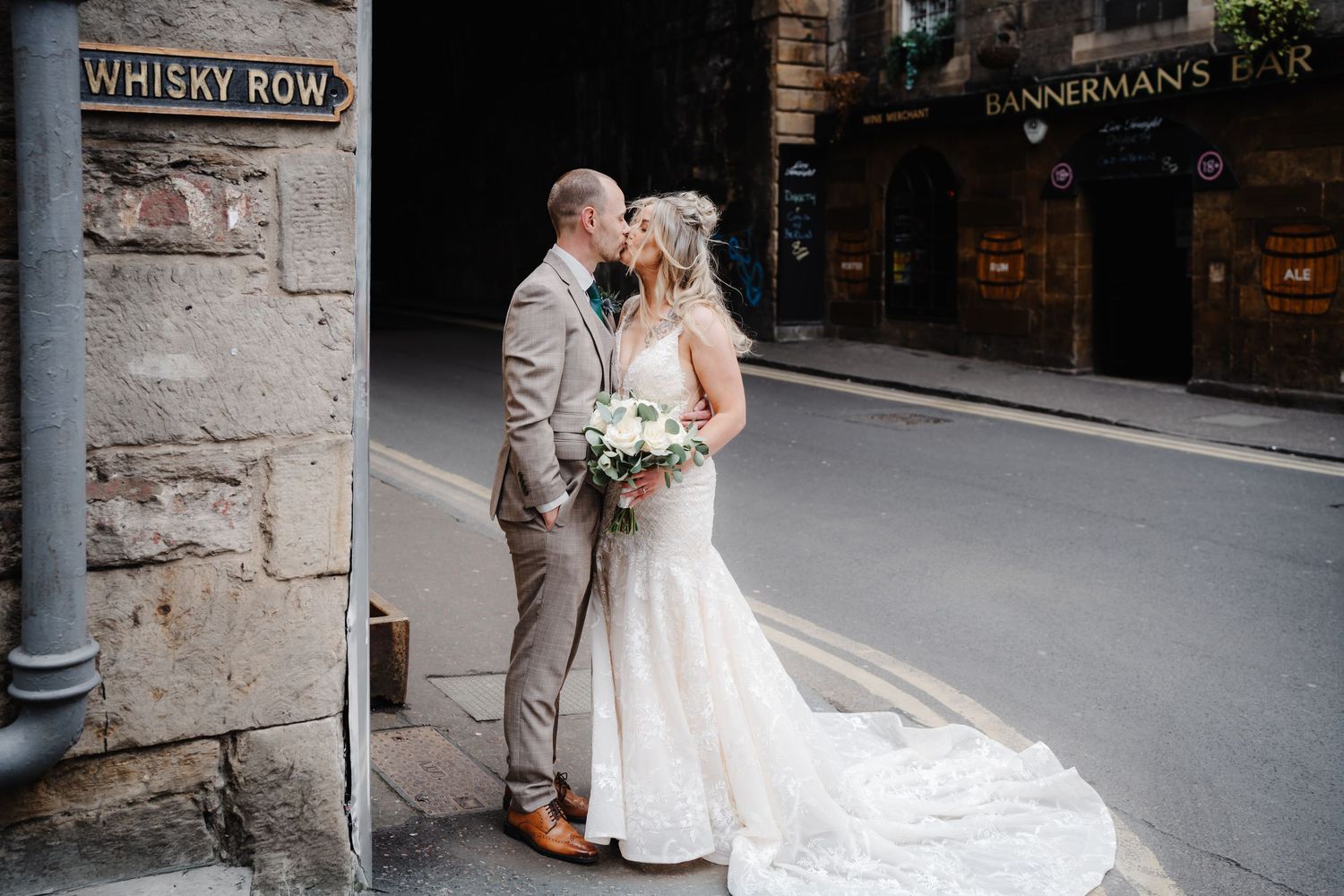 Bride and groom share a kiss on Whisky Row in Edinburgh, Scotland, with Bannermans Bar visible in the background.