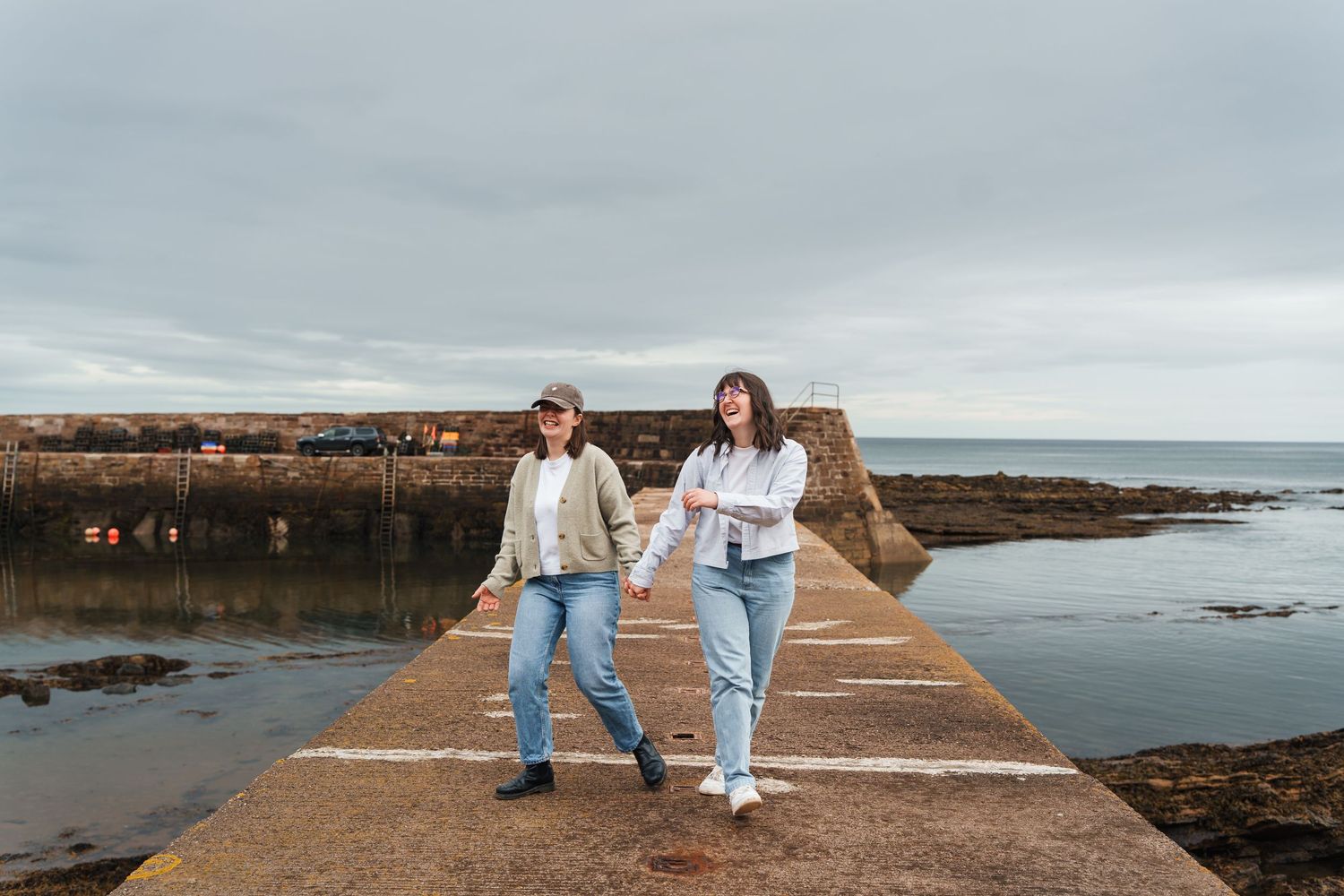 A couple walks together on a rocky coastal pathway during an overcast day at the beach.