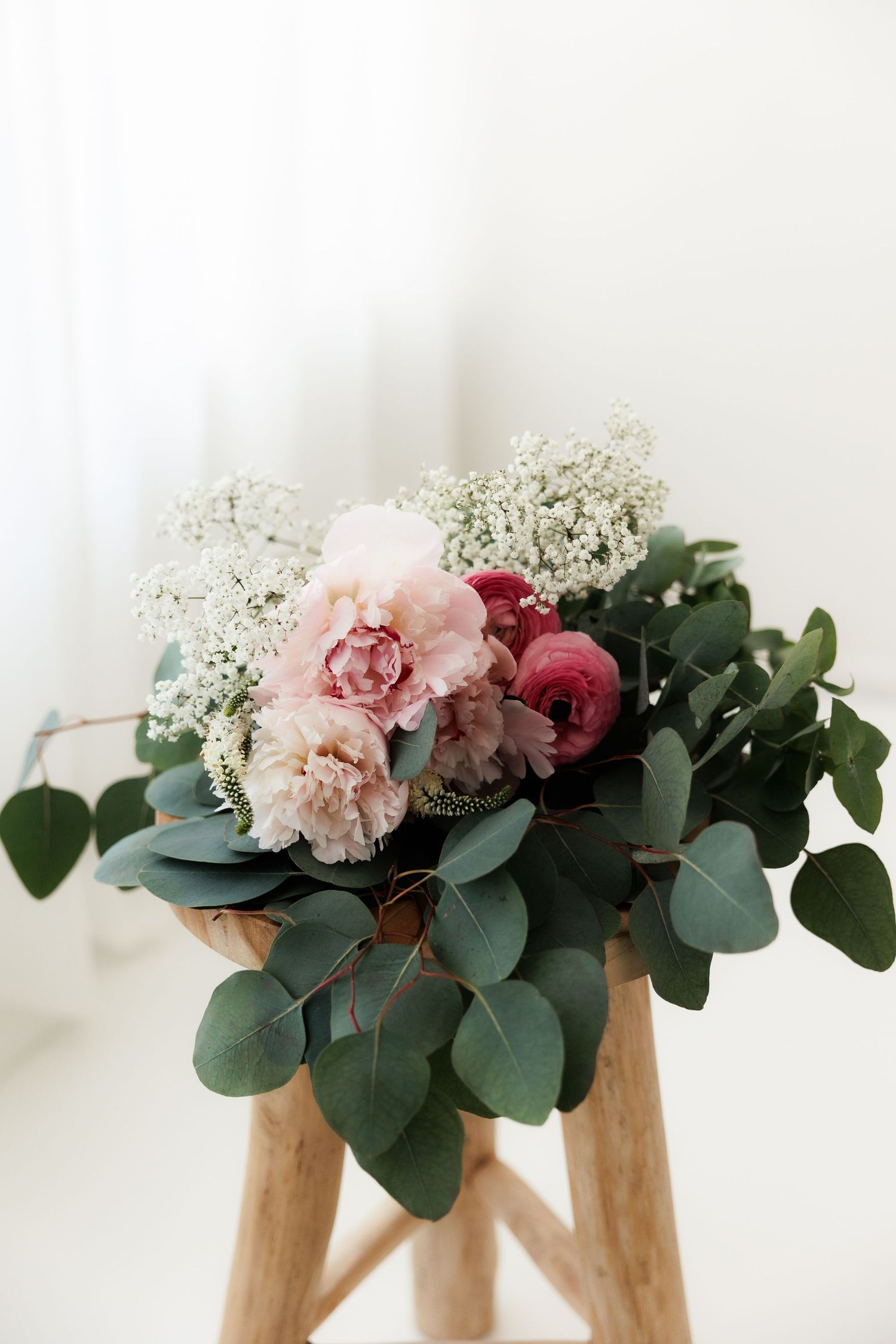 Delicate pink carnations and red roses arranged with eucalyptus leaves in wooden vases against a white background.