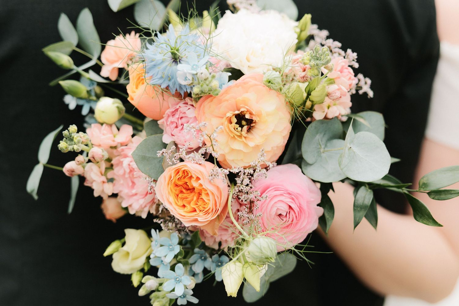 Delicate peach and pink floral bouquet with roses, ranunculus, and eucalyptus leaves arranged in a romantic garden style.