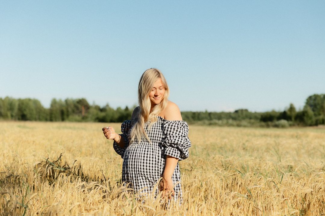 A person in a gingham shirt stands in a golden wheat field on a sunny summer day.