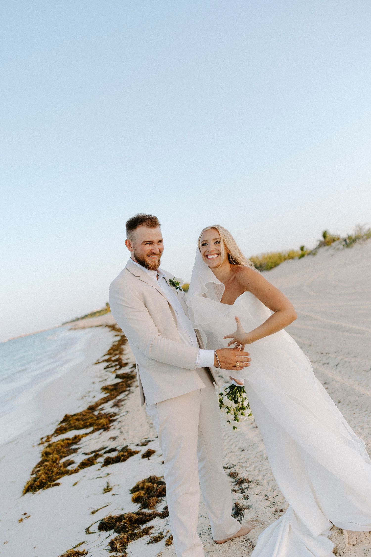 A romantic beach photoshoot featuring a couple in white attire dancing and laughing on sandy shores.