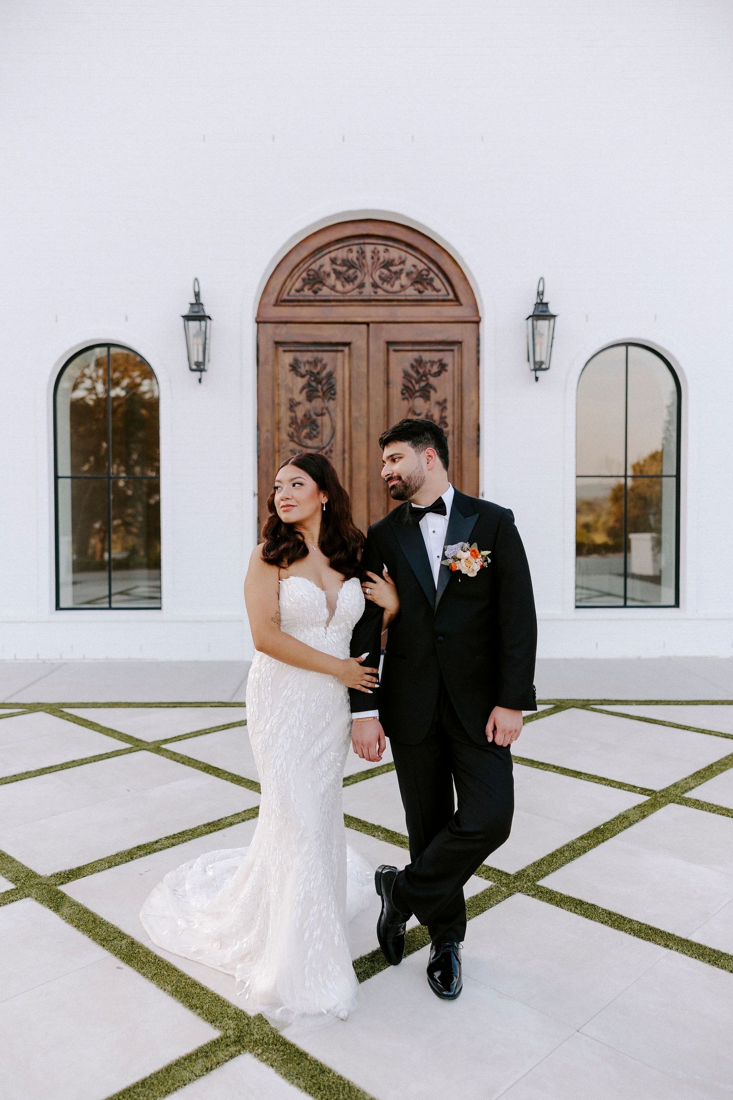 Wedding couple dancing and posing in front of a white Spanish-style building with arched doorways.
