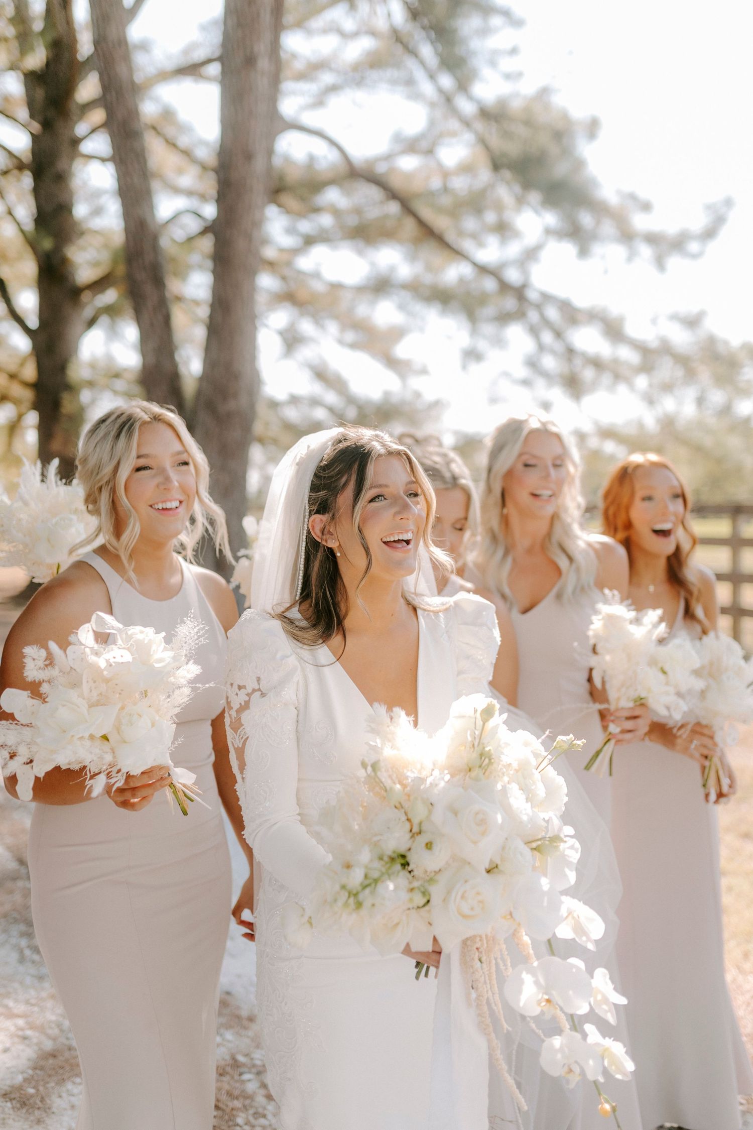 A group in white dresses laughs joyfully together while holding sparklers during an outdoor celebration.