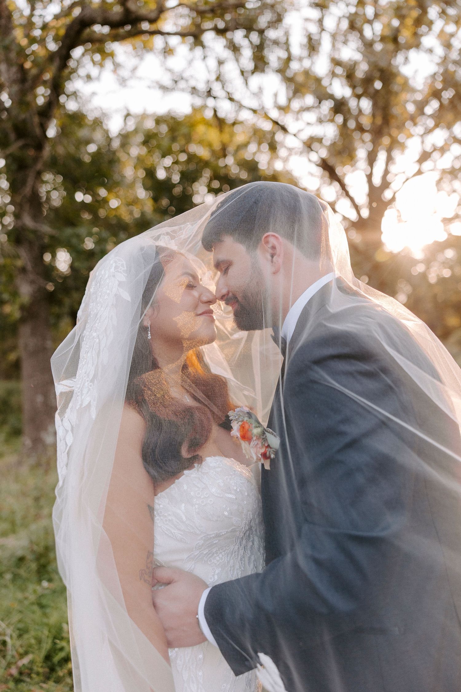 Romantic wedding photos of a couple sharing intimate moments under a flowing veil at sunset.