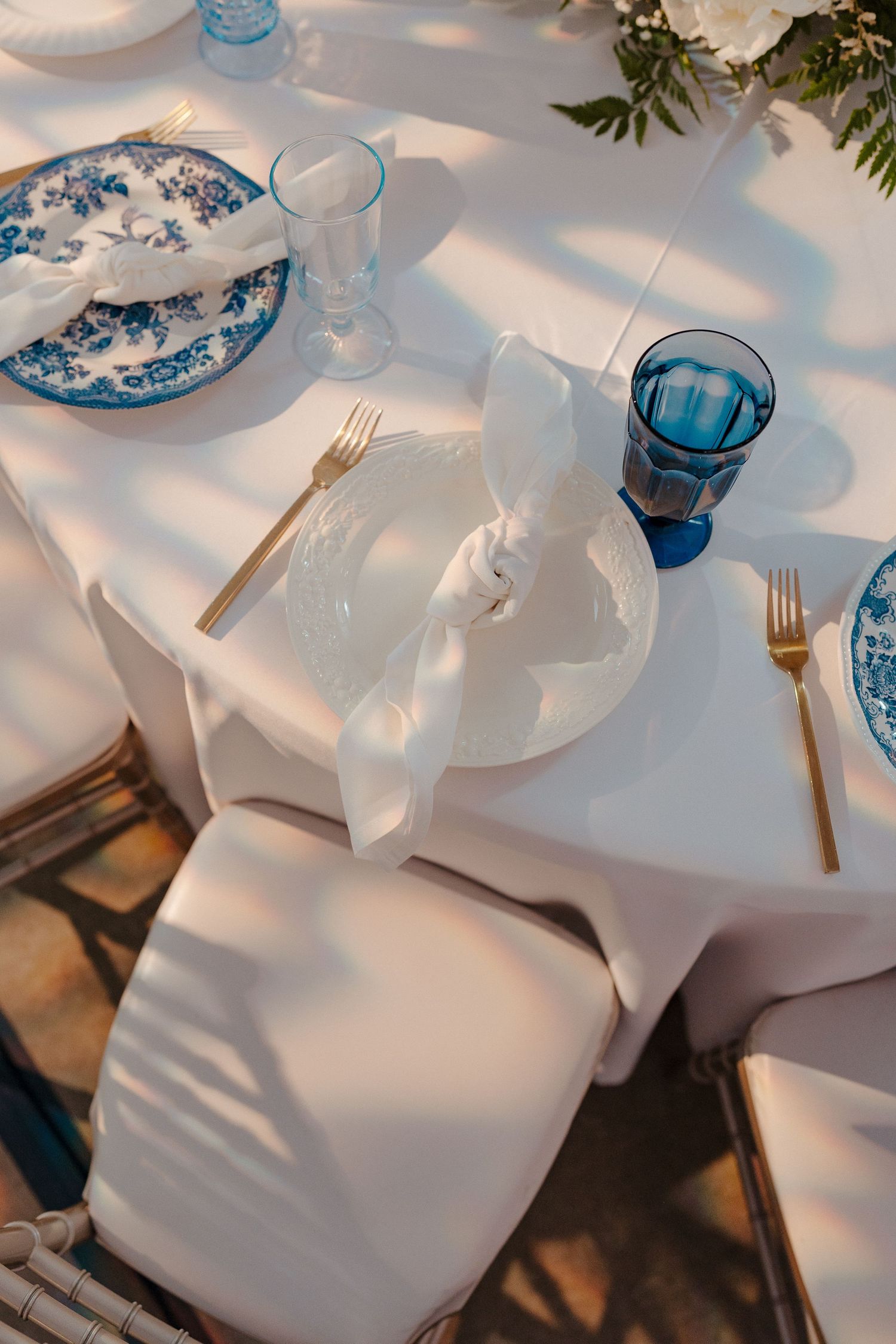Elegant table setting with white linens and blue glassware creating a sophisticated dining atmosphere.