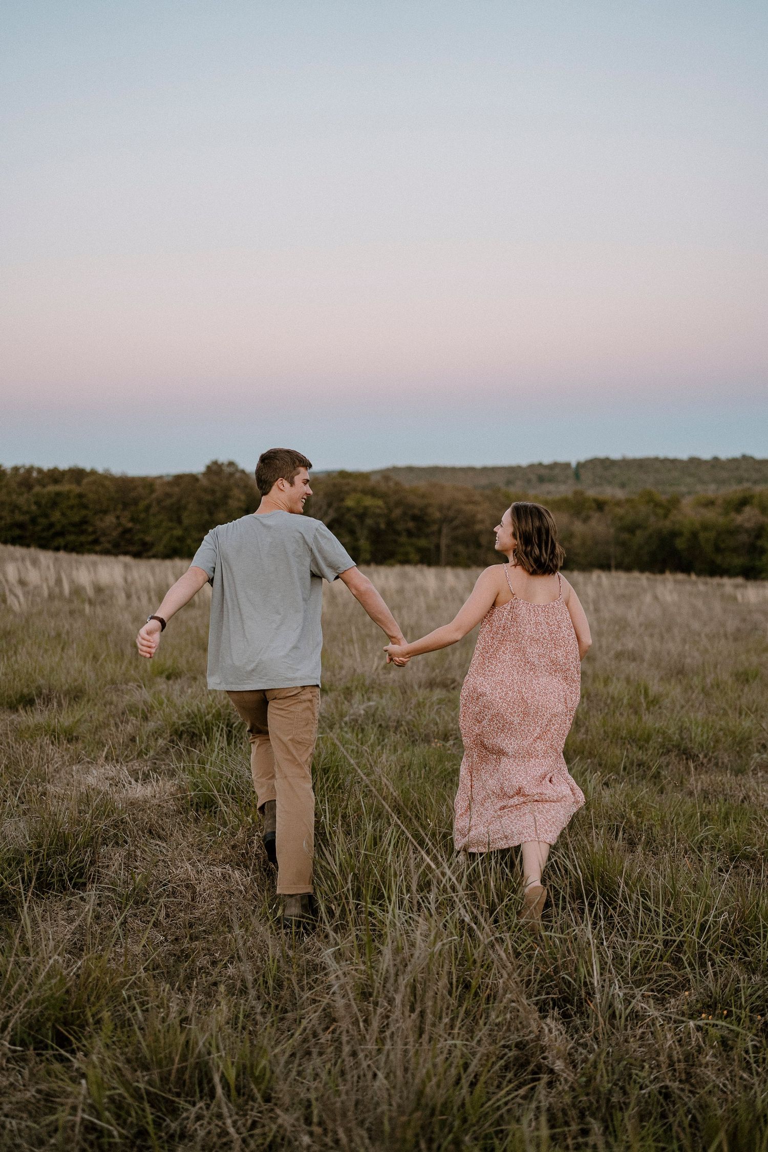 Couple walking hand in hand through a scenic field at sunset.
