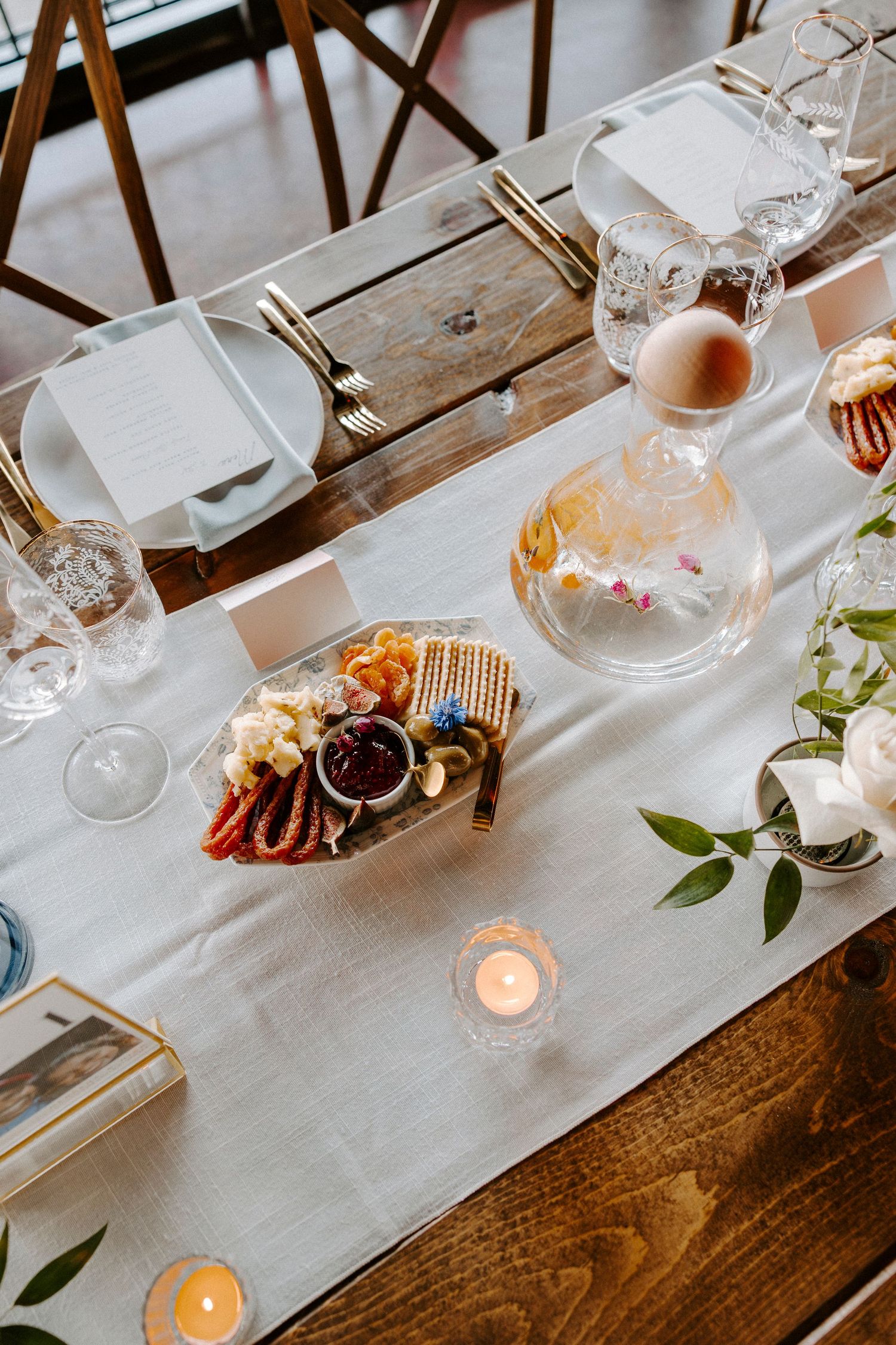 Elegant table setting with white linens, glowing candles, and wine glasses on a rustic wooden dining table.