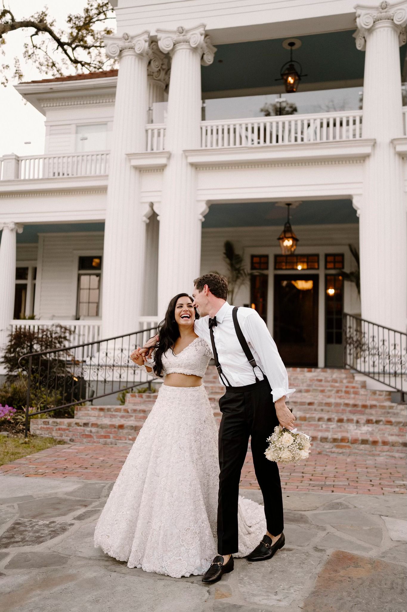 Wedding couple dancing playfully outside historic white columned mansion.