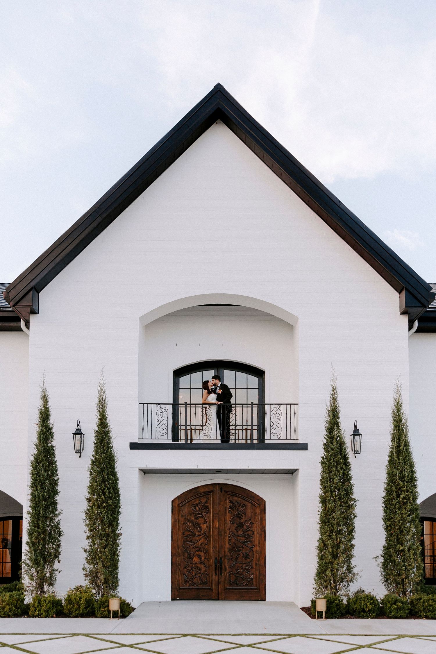 Modern white church building exterior with arched wooden doors and cypress trees lining the facade.