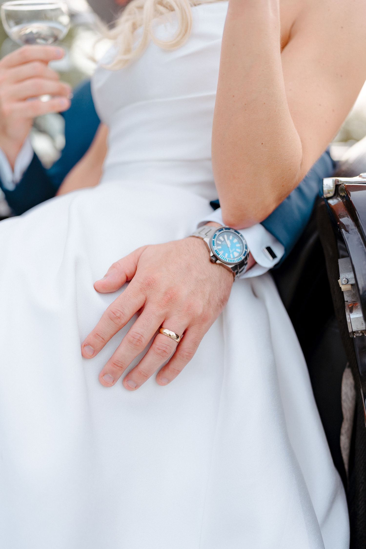 Close-up details of wedding rings and formal attire in white.