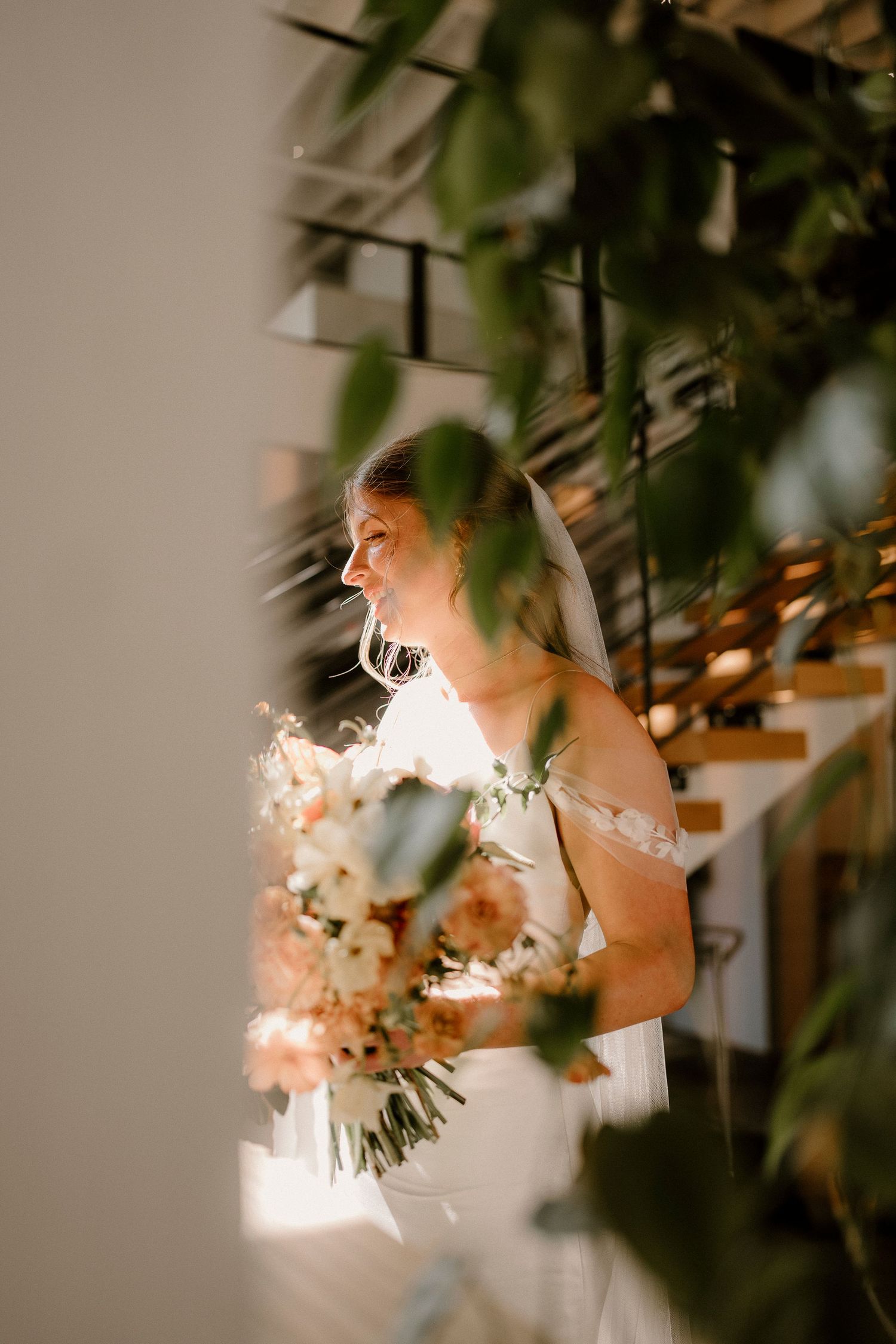 Ethereal bridal portrait through foliage with soft natural lighting and floral bouquet.