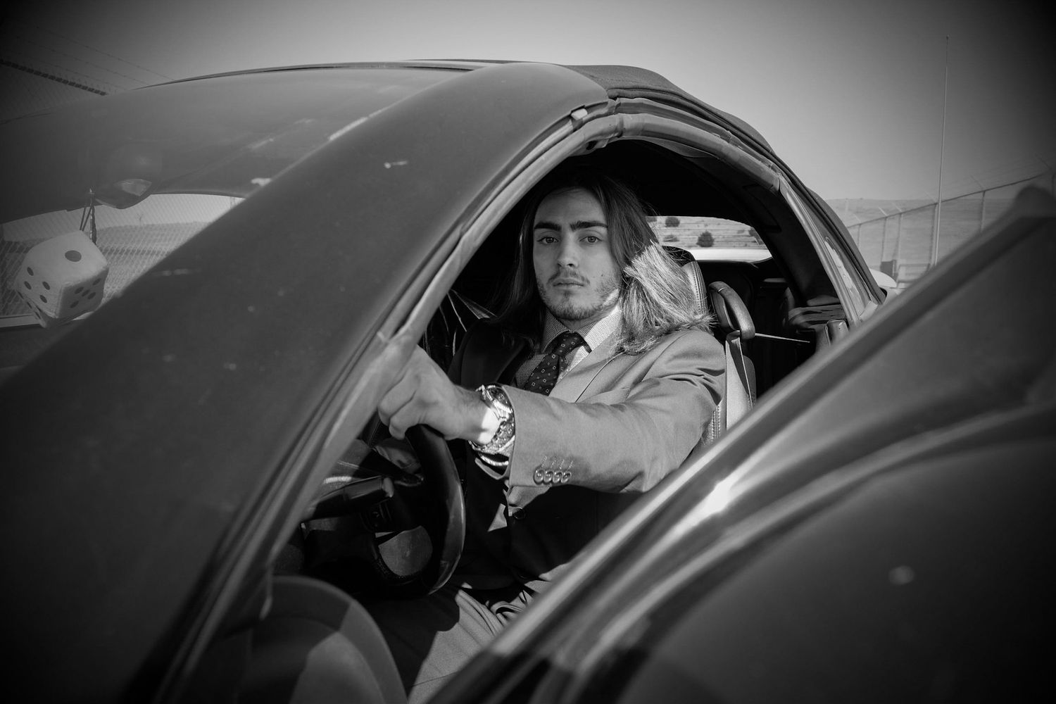 A person is sitting in the driver's seat of a vehicle, with a serious expression on their face.