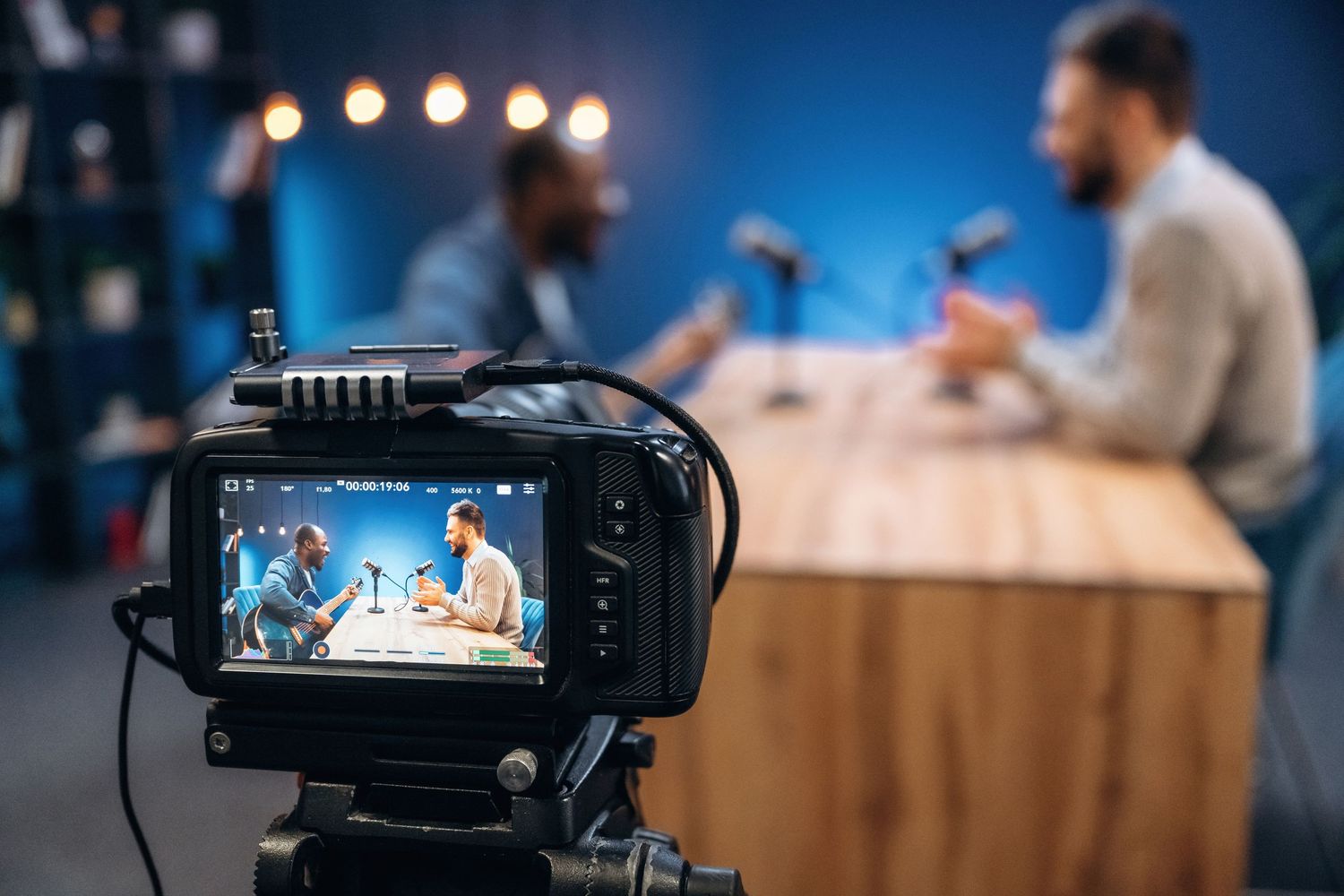 Professional video camera recording interview setup in modern office with studio lighting and microphones.