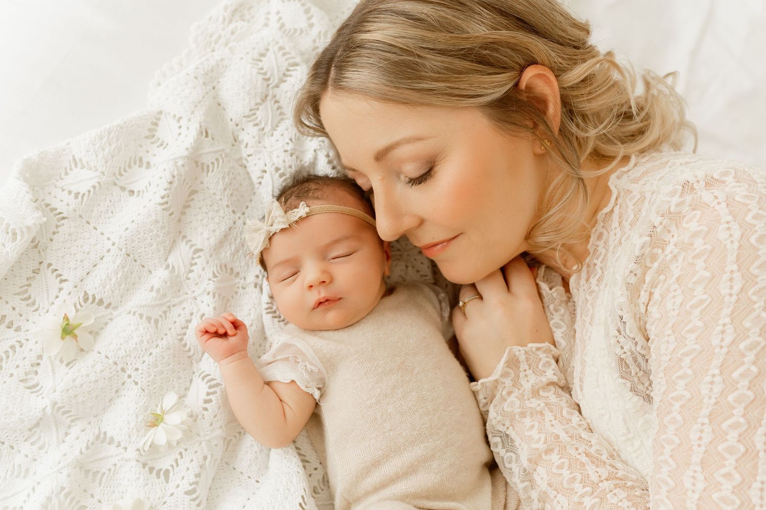 A tender moment captured between mother and sleeping newborn on white lace bedding.
