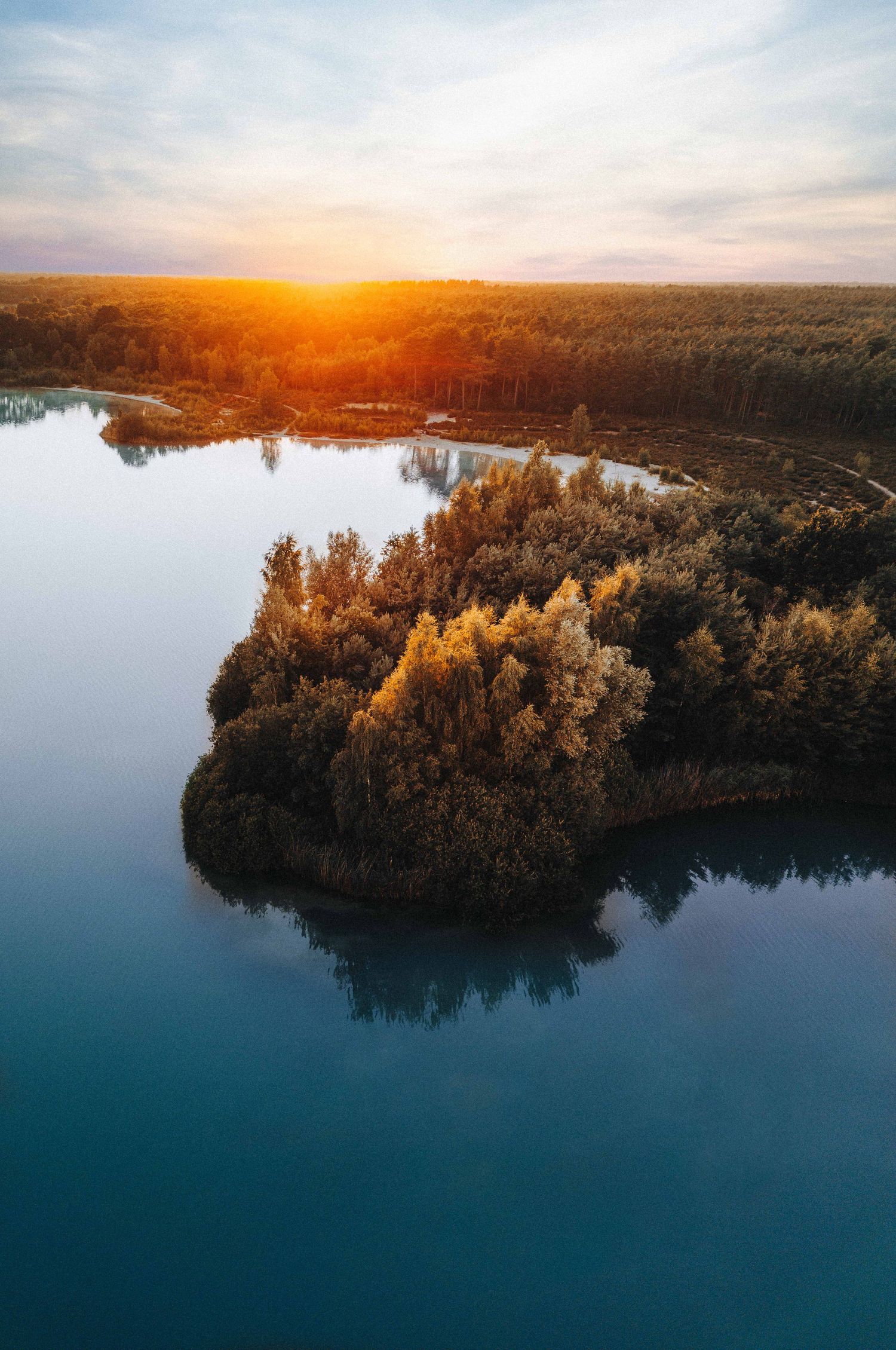 Zonsondergang boven meer met eiland vol bomen en reflecties in het water. Nederheide, Noord-Brabant. Nederland.