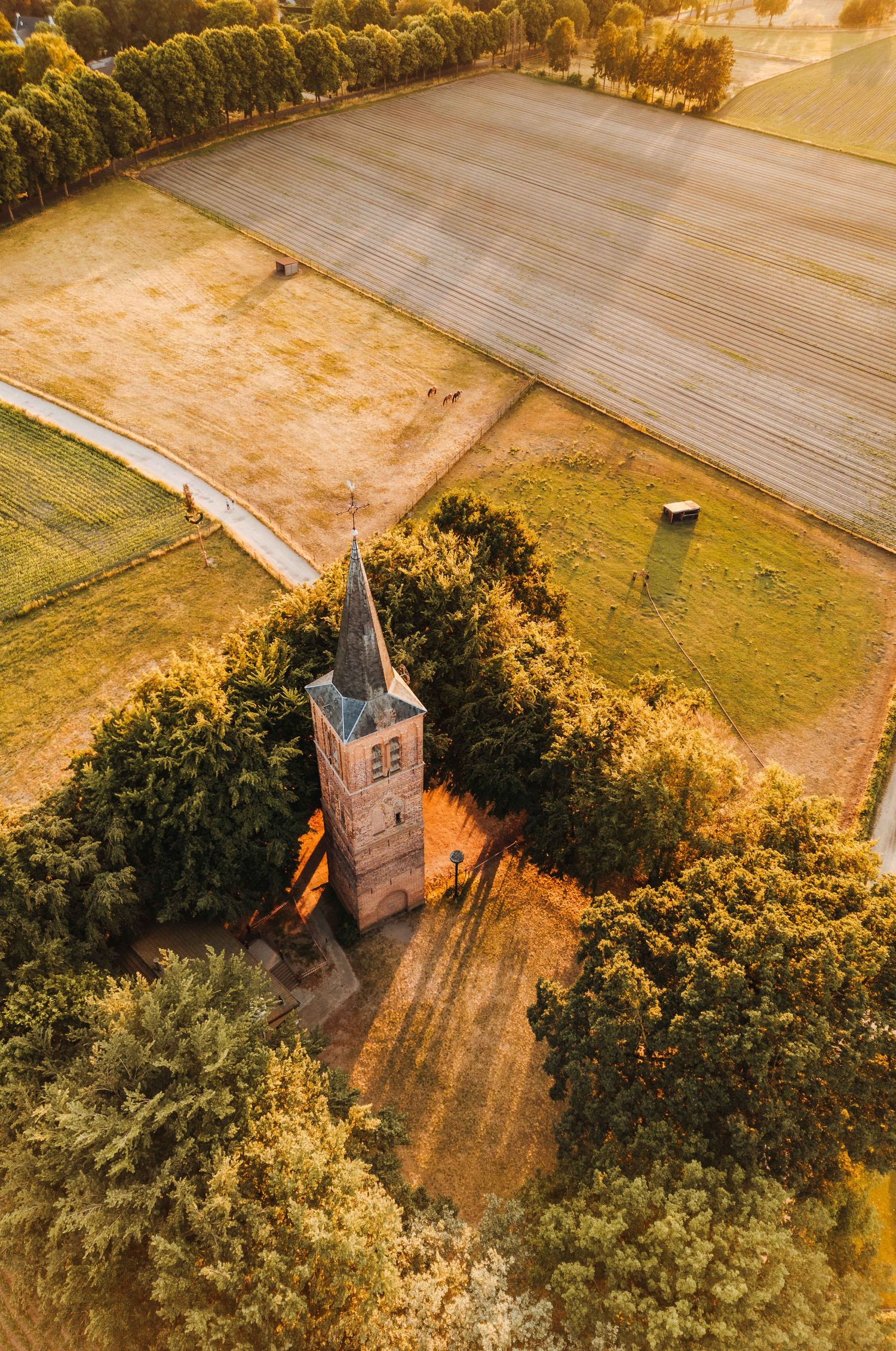 Dronefoto van kerktoren midden in een veld bij zonsopkomst te Stiphout, Noord-Brabant. Nederland.