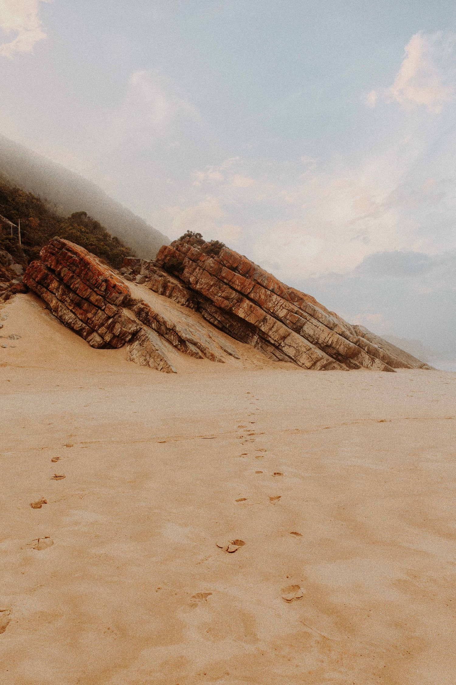 Voetstappen op een verlaten zandstrand bij rotsformatie