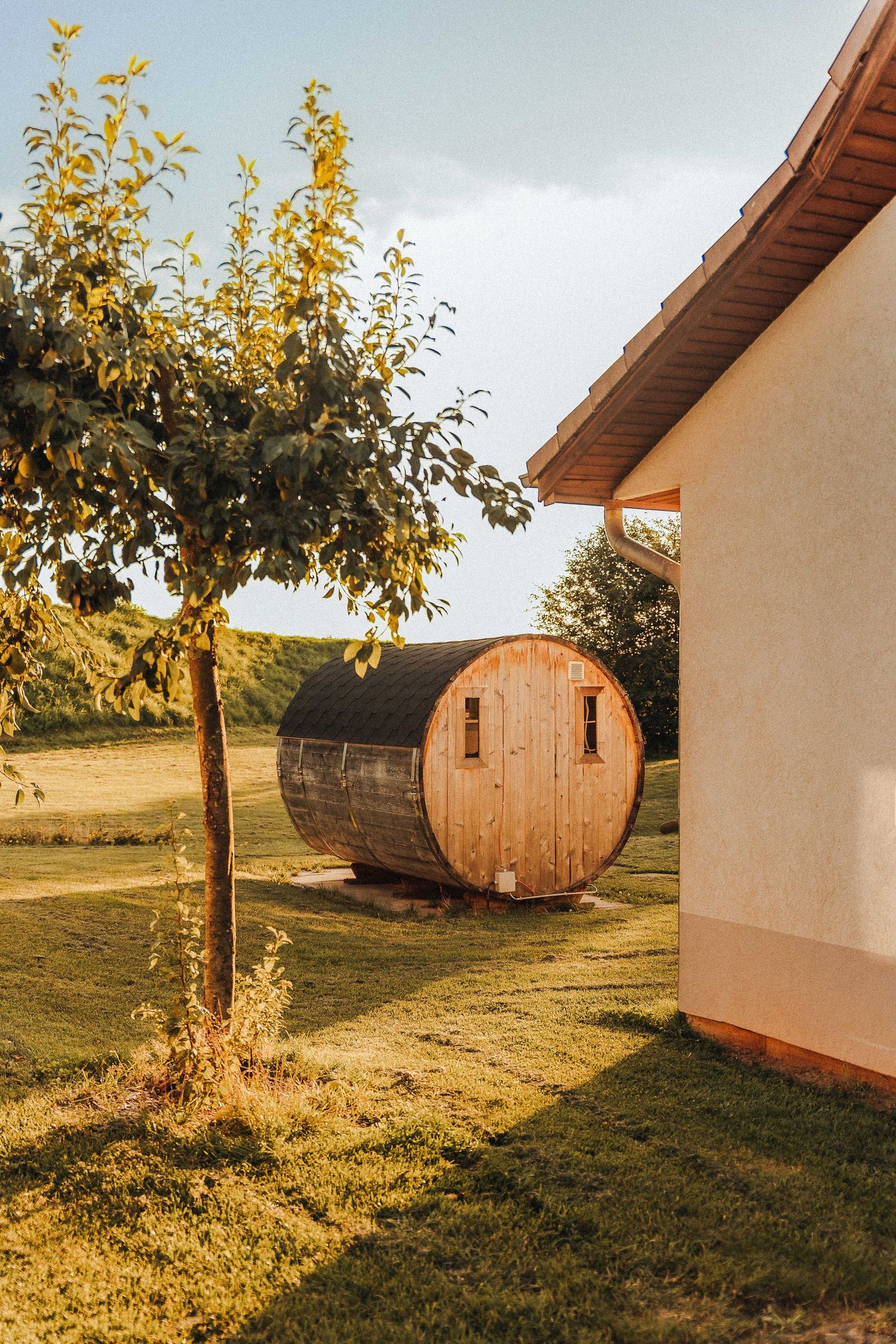 Houten sauna op grasveld naast een wit huis onder een boom bij Roompot park Cochem.