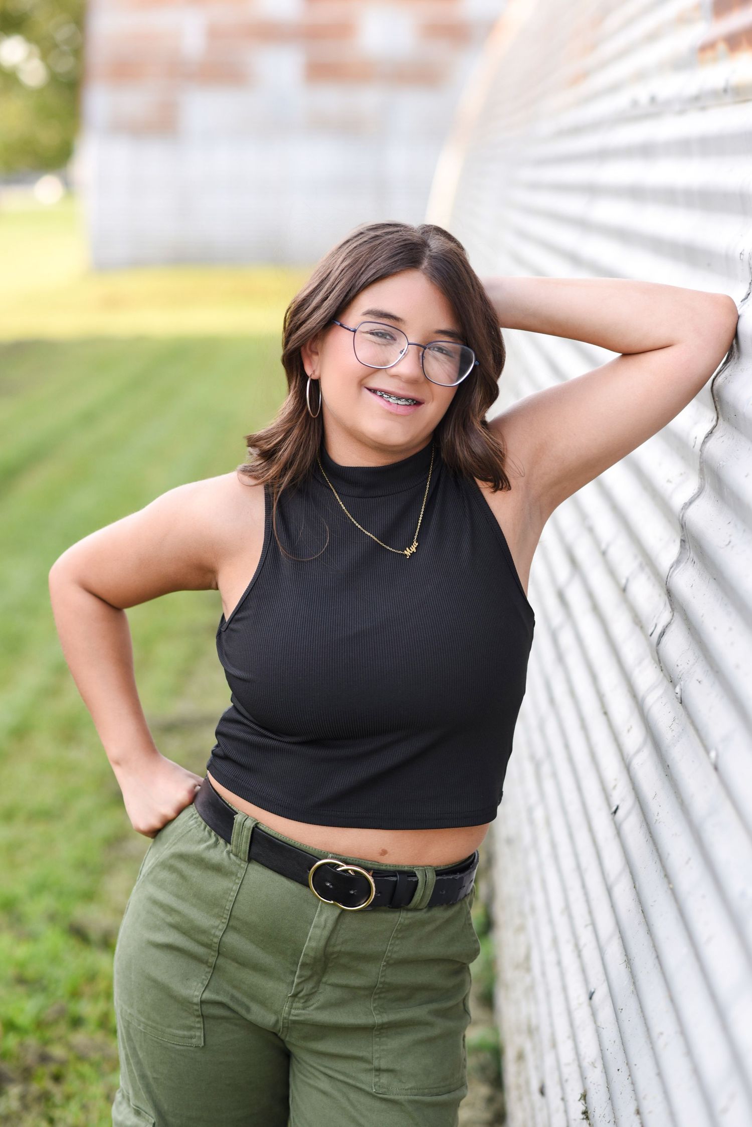 Young woman standing and smiling an outdoor photoshoot leaning up against a buliding in Gretna NE.