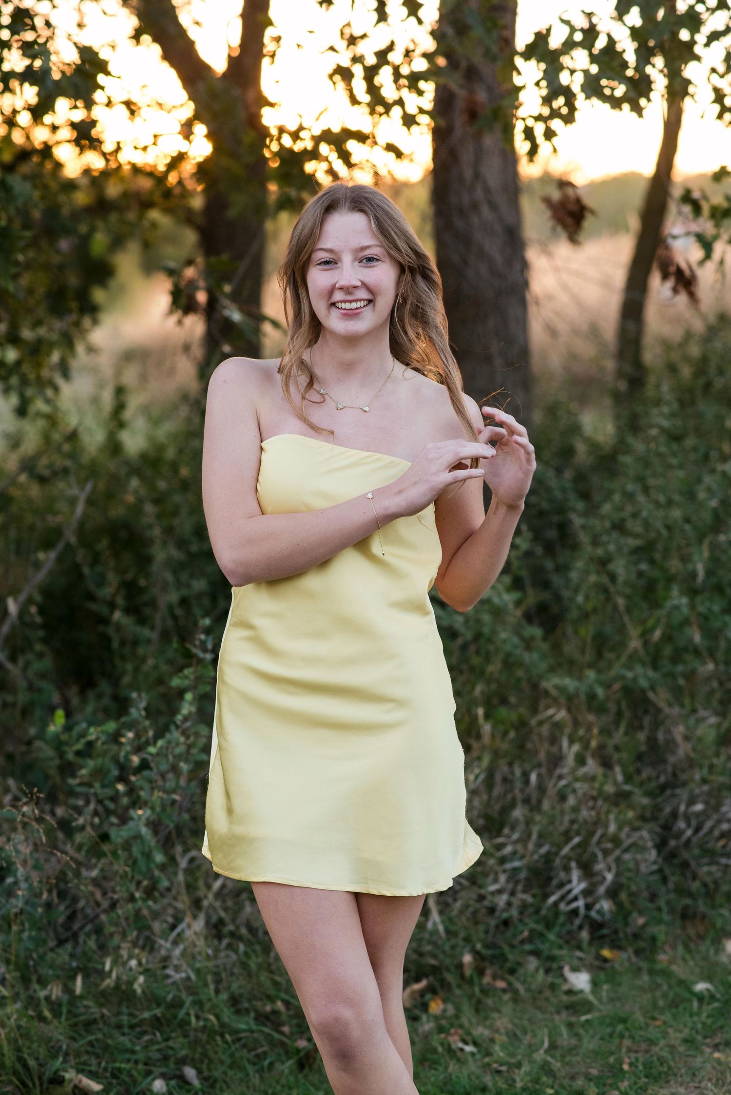 Young woman standing and smiling an outdoor photoshoot in trees.