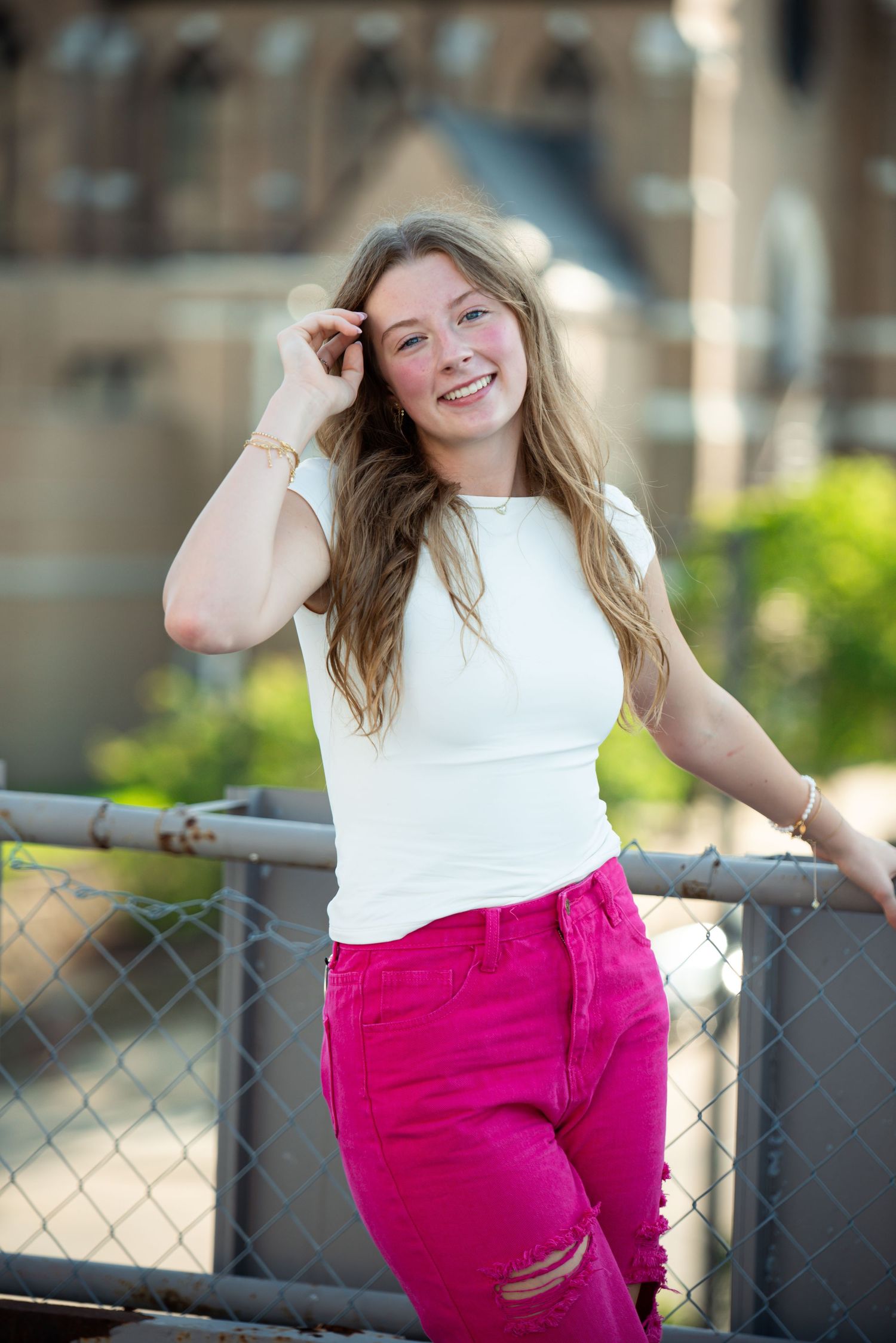 Young woman standing and smiling while touching her hair during an outdoor photoshoot in Omaha, NE. She is on a roof top.