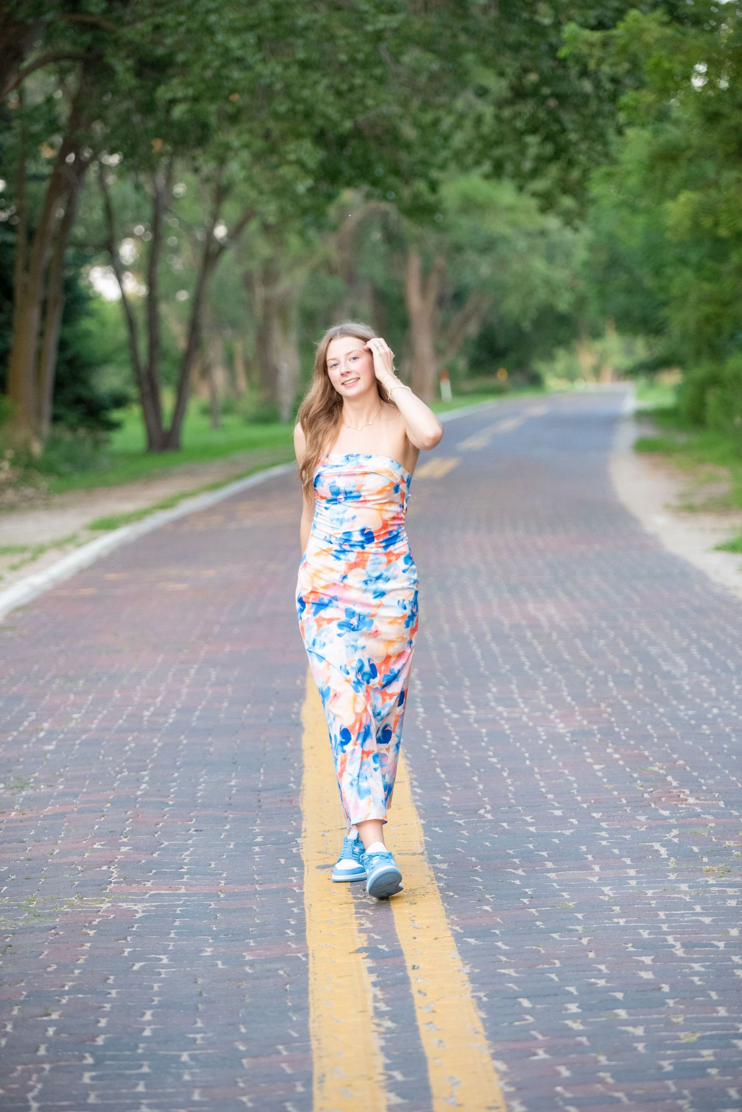 Young woman standing and smiling while touching her hair during an outdoor photoshoot in Omaha, NE. She is on an old brick road.