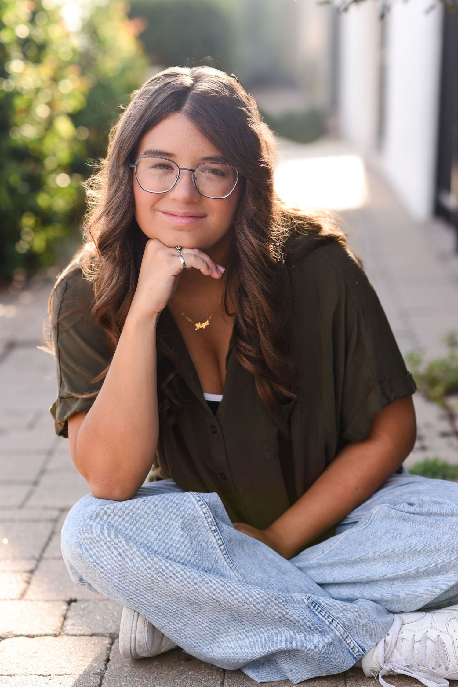 Young woman sitting and smiling an outdoor photoshoot leaning up against a building in Gretna NE.