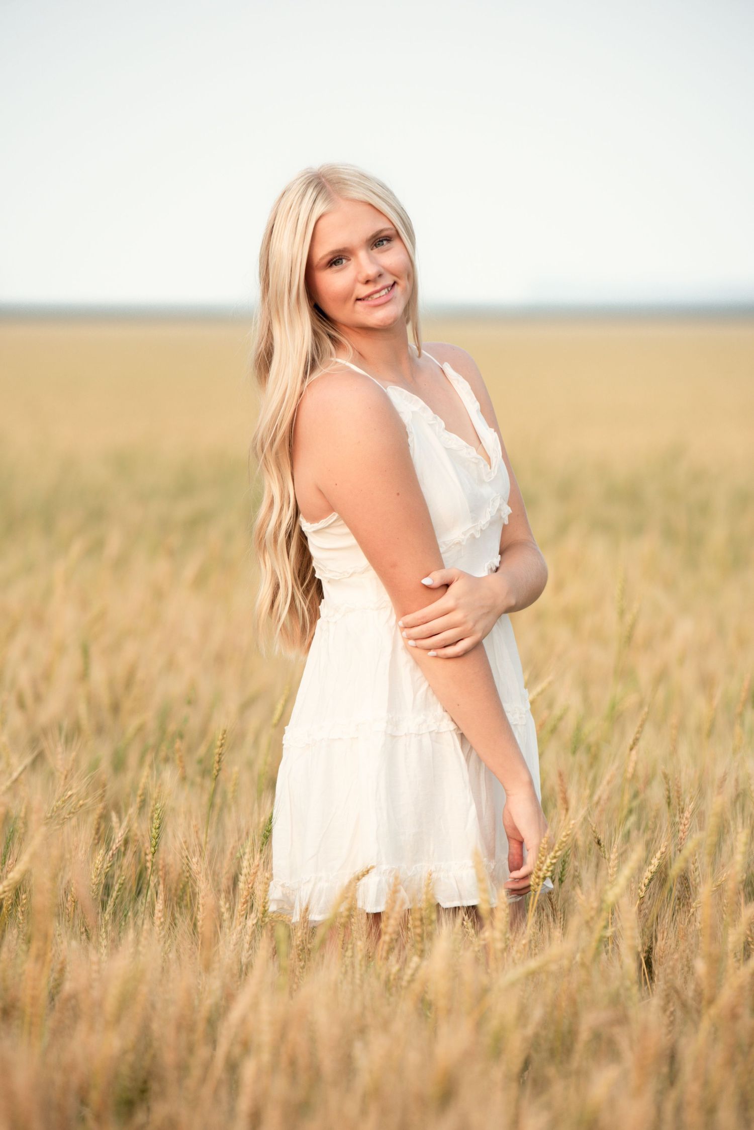 Young woman standing  in a wheat field and smiling during an outdoor photoshoot in Omaha, NE.
