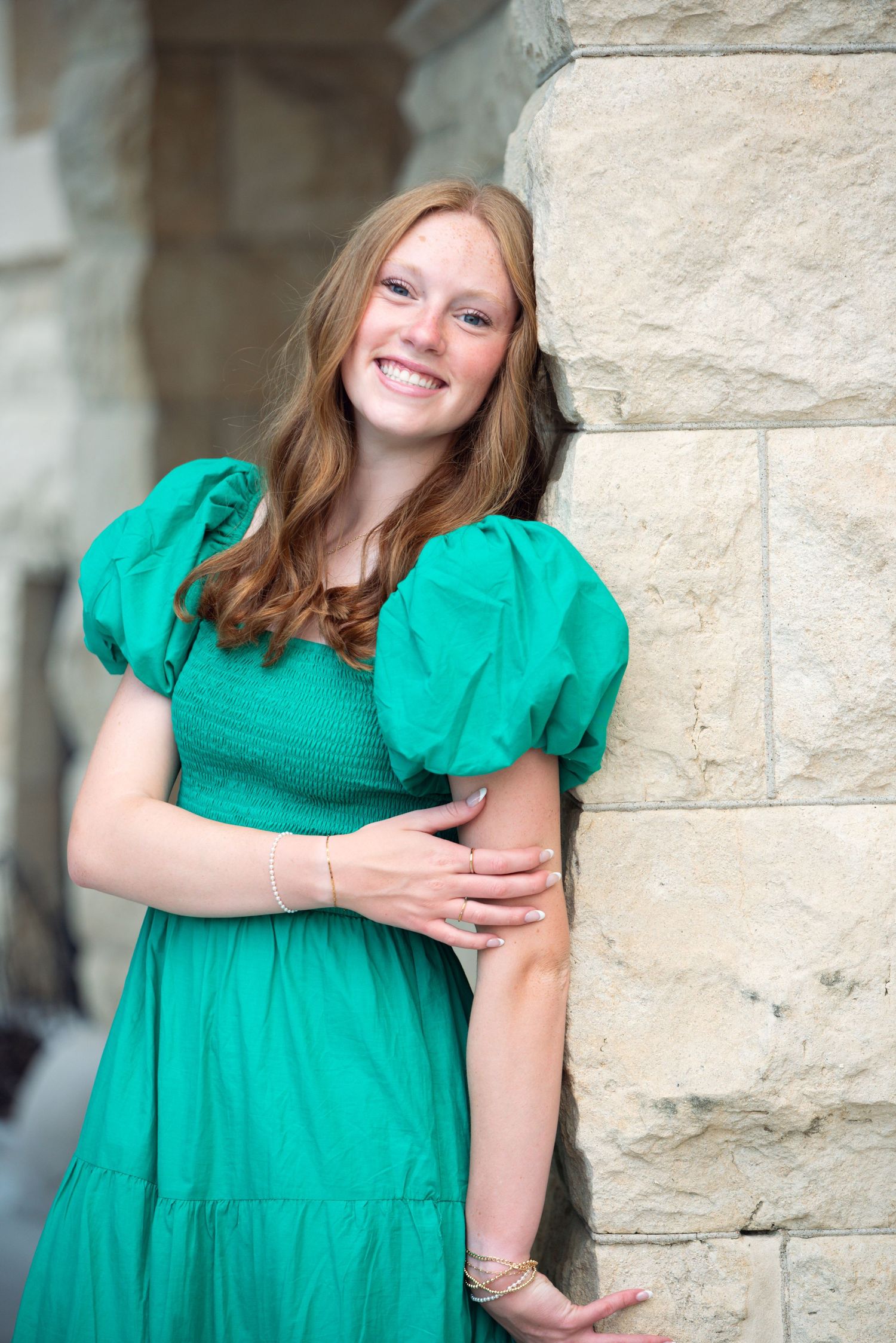 Young woman standing and smiling an outdoor photoshoot  at Joselyn Castle in Omaha, NE. She is on a roof top.
