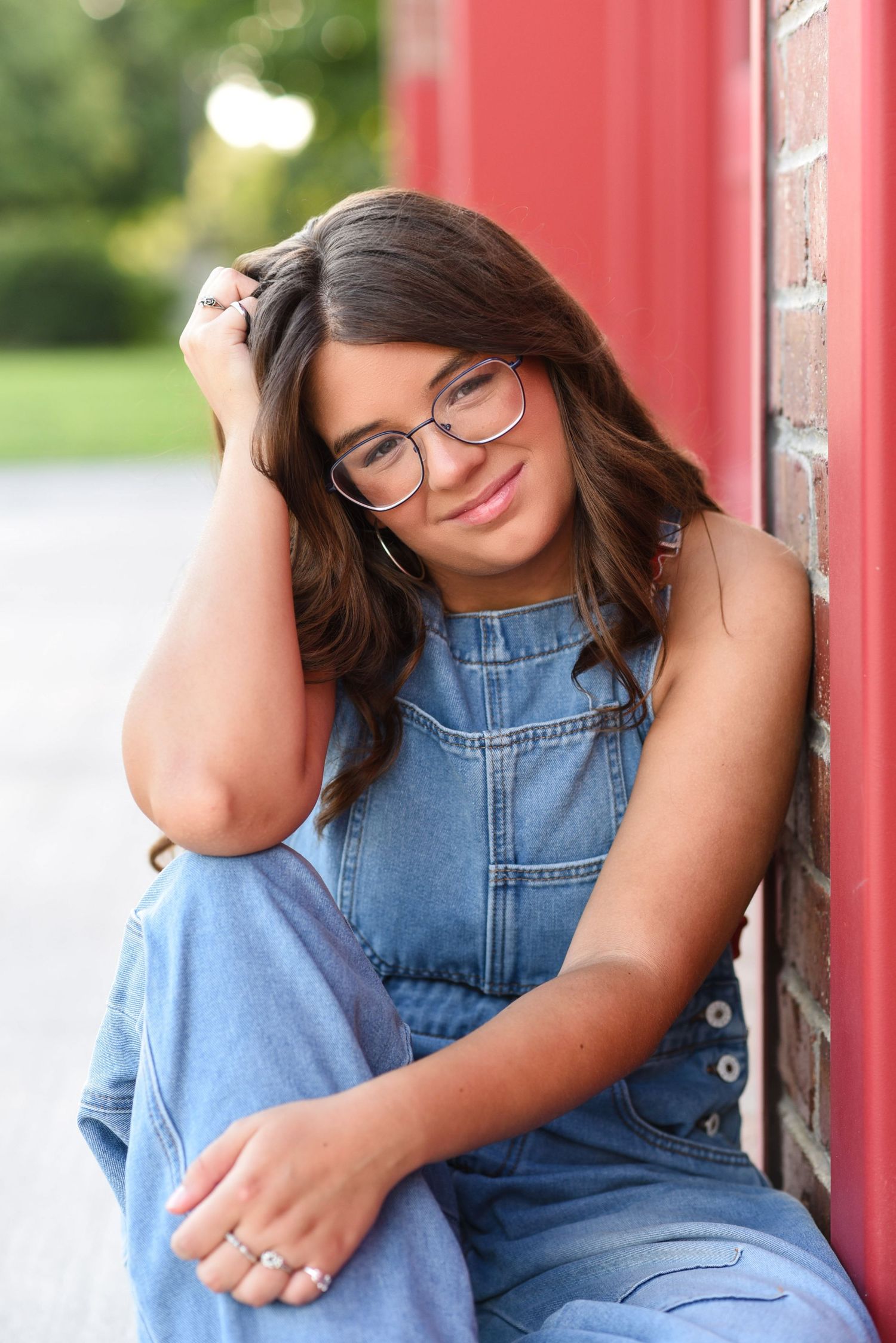 Young woman standing and smiling an outdoor photoshoot leaning up against a red buliding in Gretna NE.