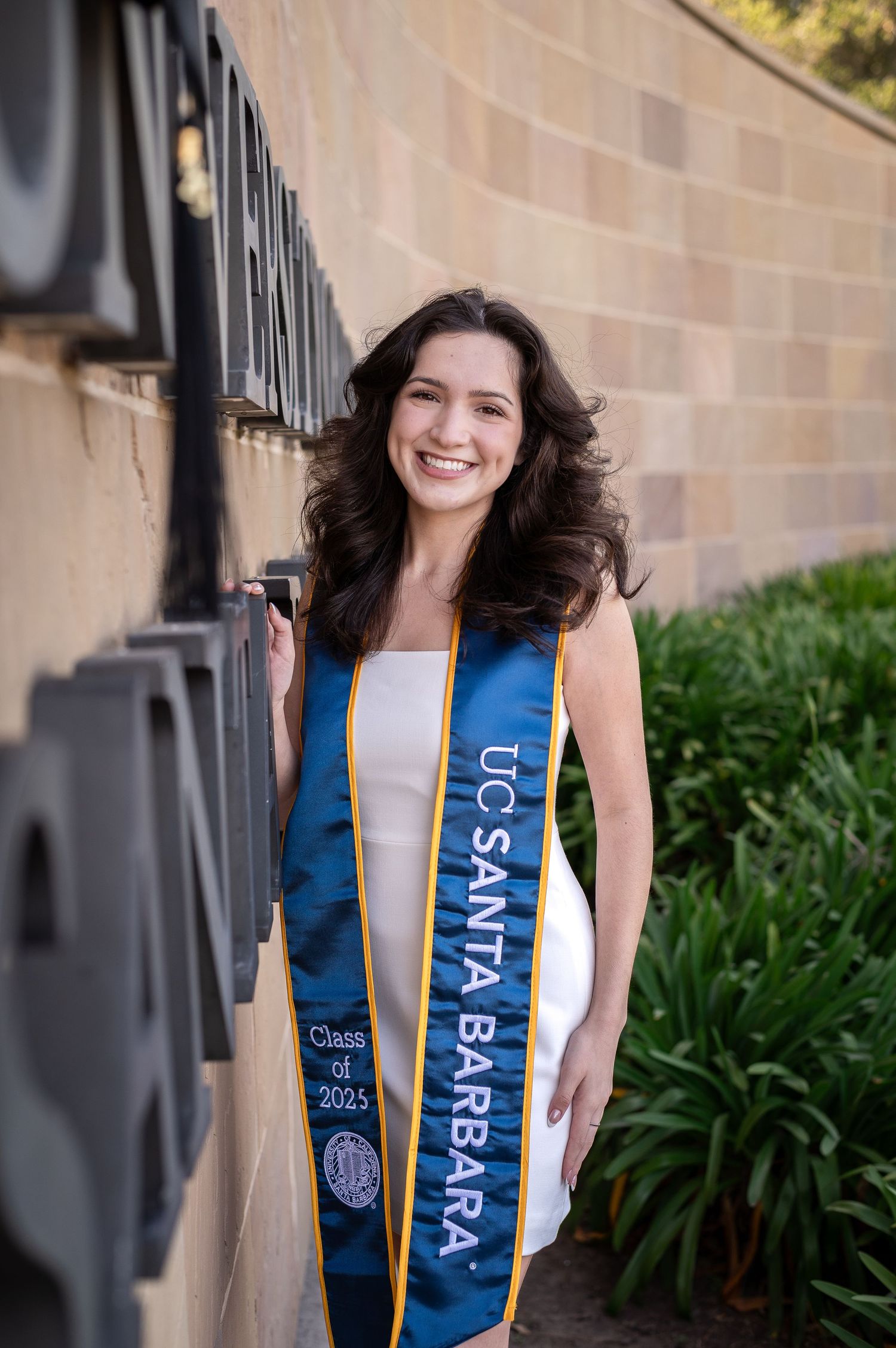 Graduate student in blue academic stole posing against brick wall for graduation photos in a sequence of four shots.