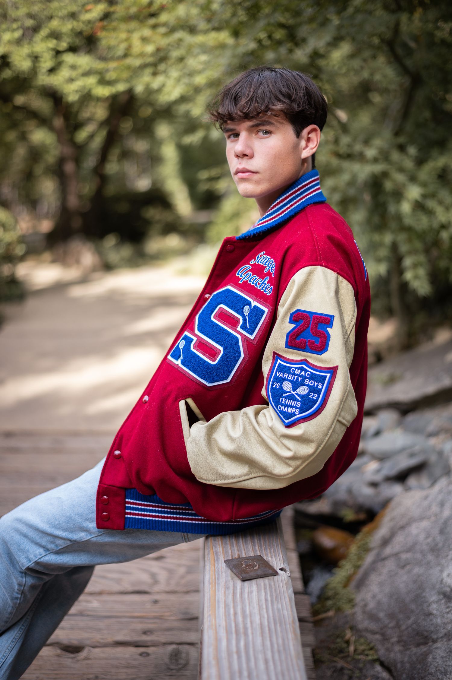 A varsity letterman jacket in red and cream with USA patches displayed on a wooden bridge in an outdoor setting.