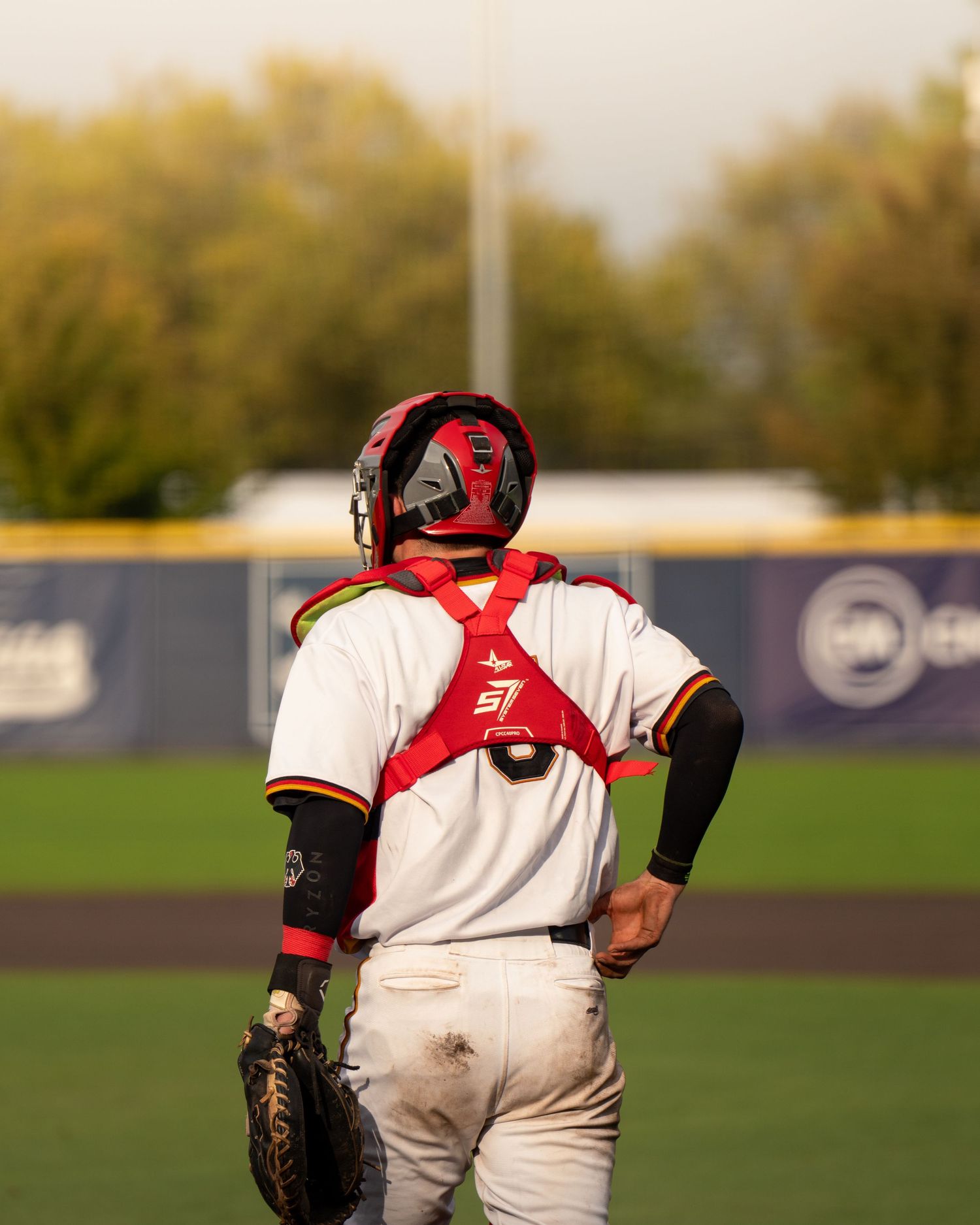Baseball catcher crouches in ready position behind home plate during game at sunset.