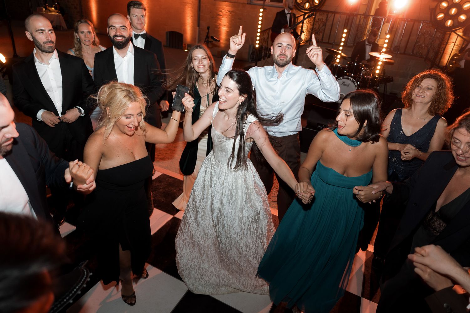 Guests dancing joyfully at an elegant wedding reception on a black and white checkered dance floor.