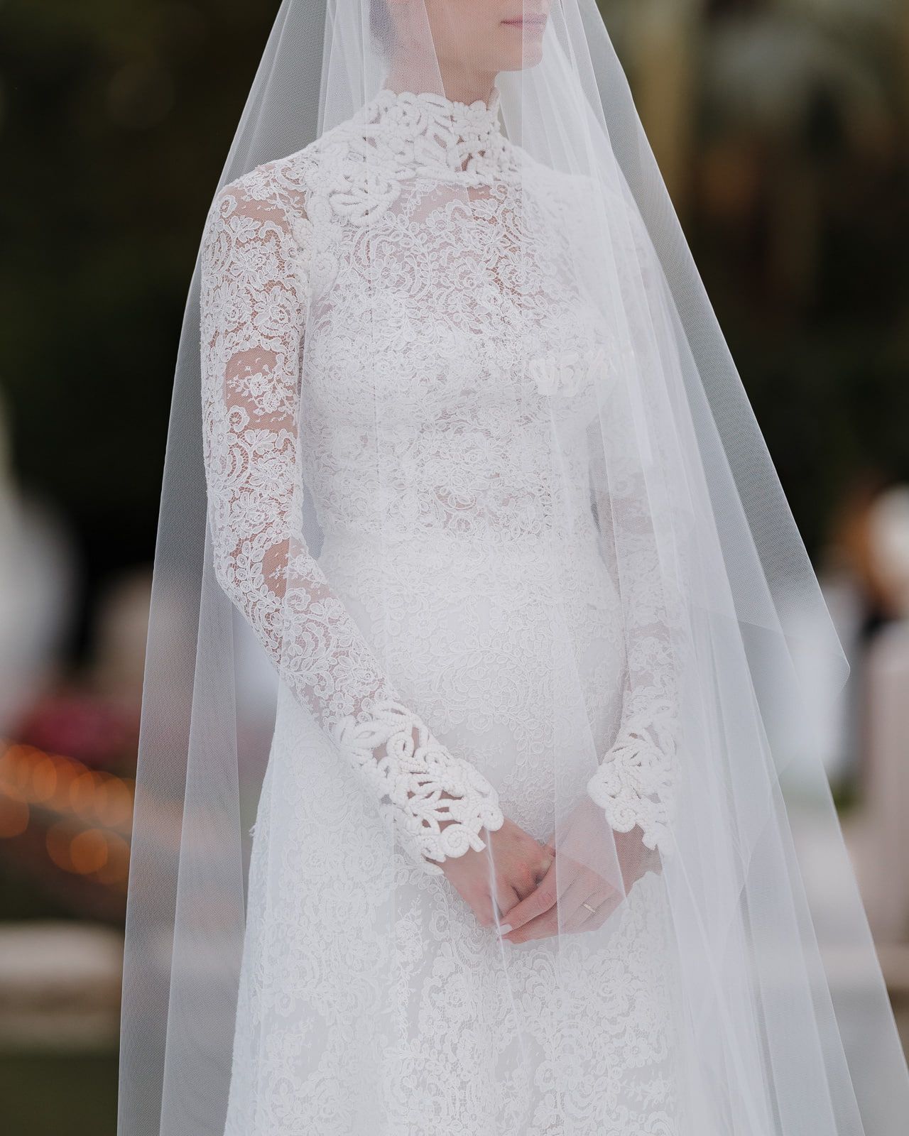 Close-up details of a delicate white lace wedding dress with long sleeves and veil.