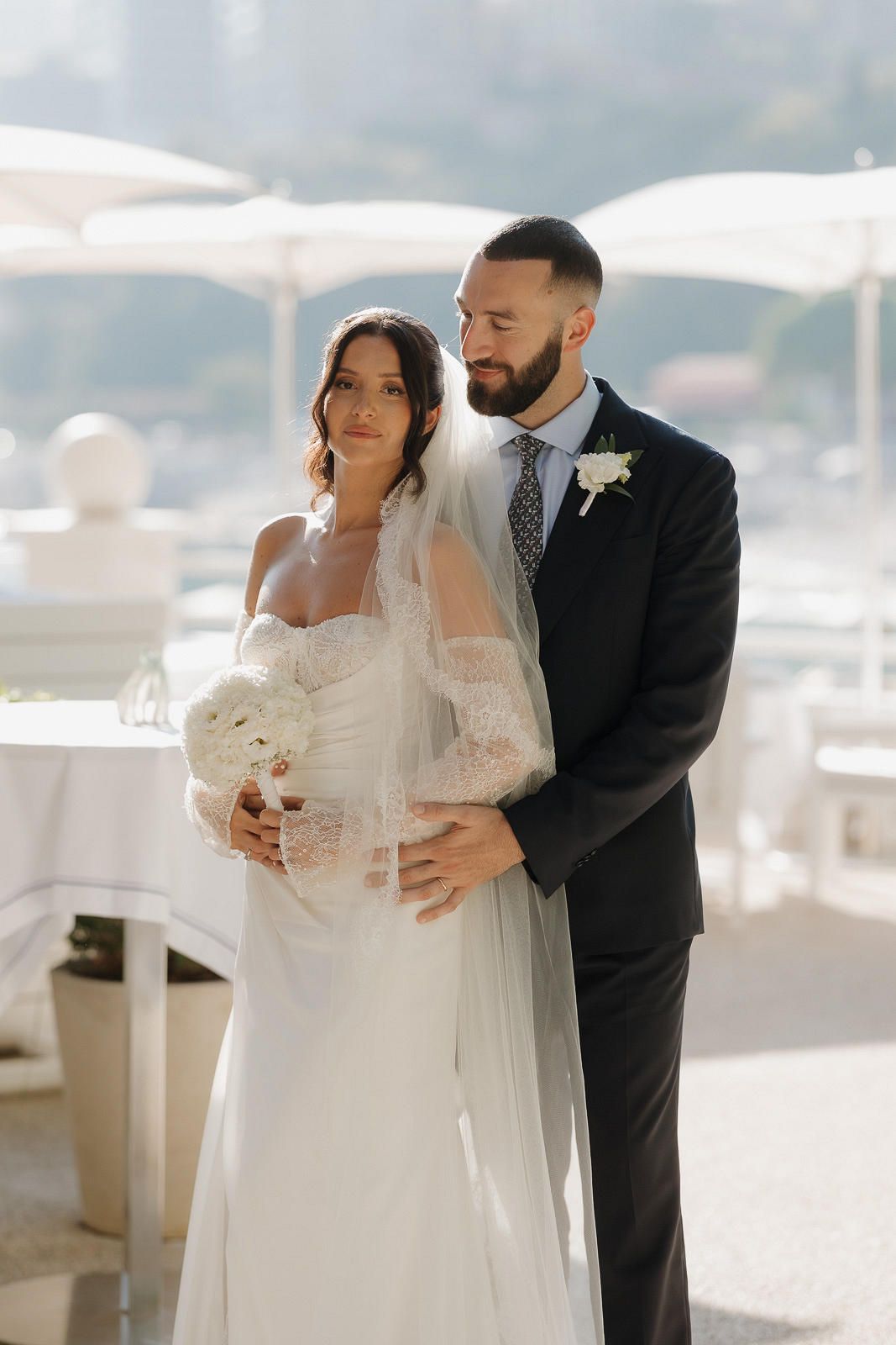 A romantic wedding couple embraces on a bright sunny terrace overlooking a scenic waterfront view.