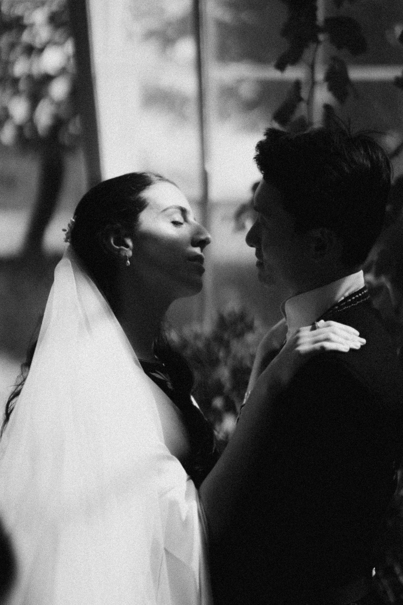 Elegant black and white wedding portrait of bride in veil leaning toward groom.